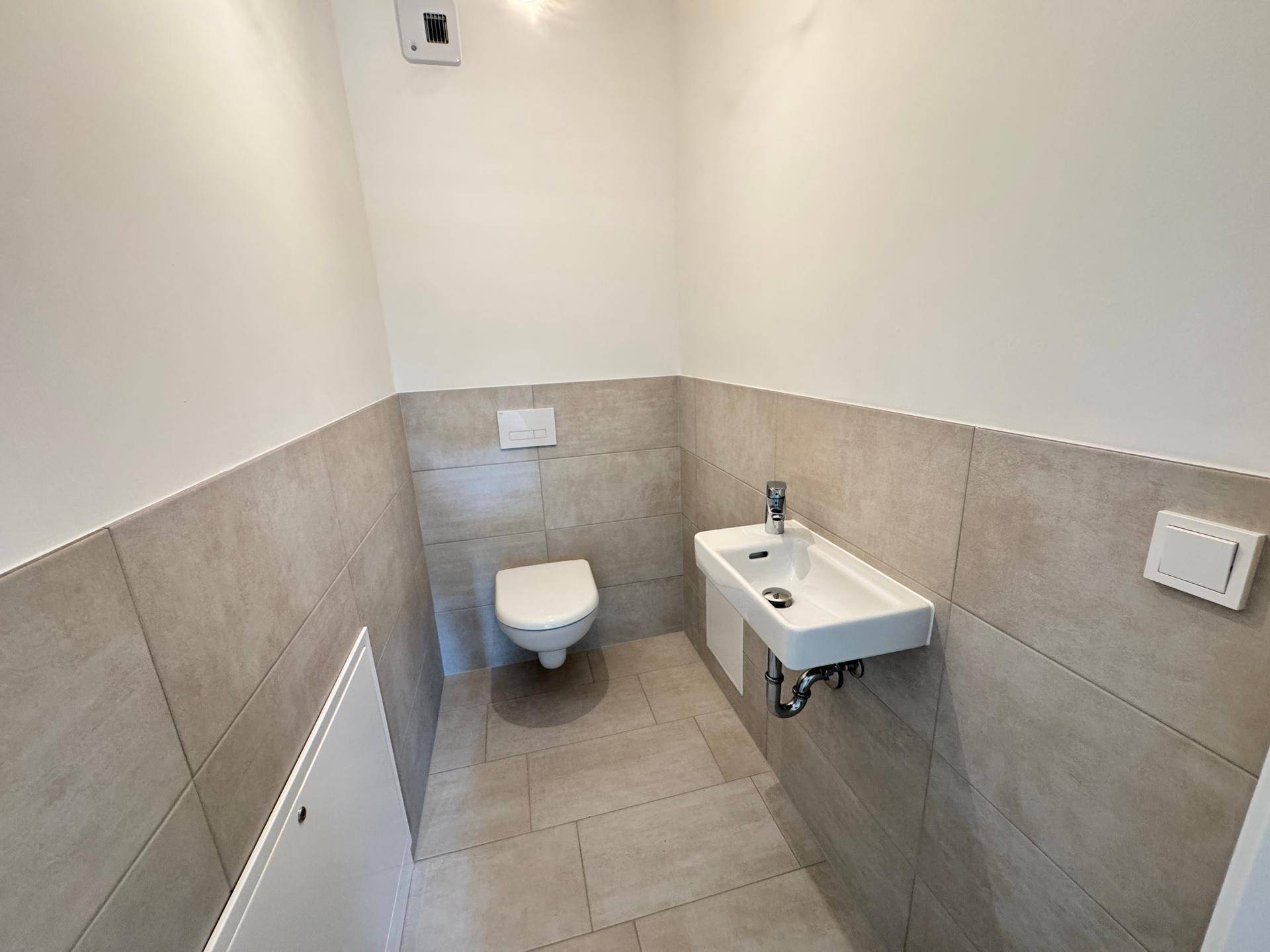 Modernes Gäste-WC mit Wand-WC und kleinem Waschbecken, hell gefliest und funktional.
