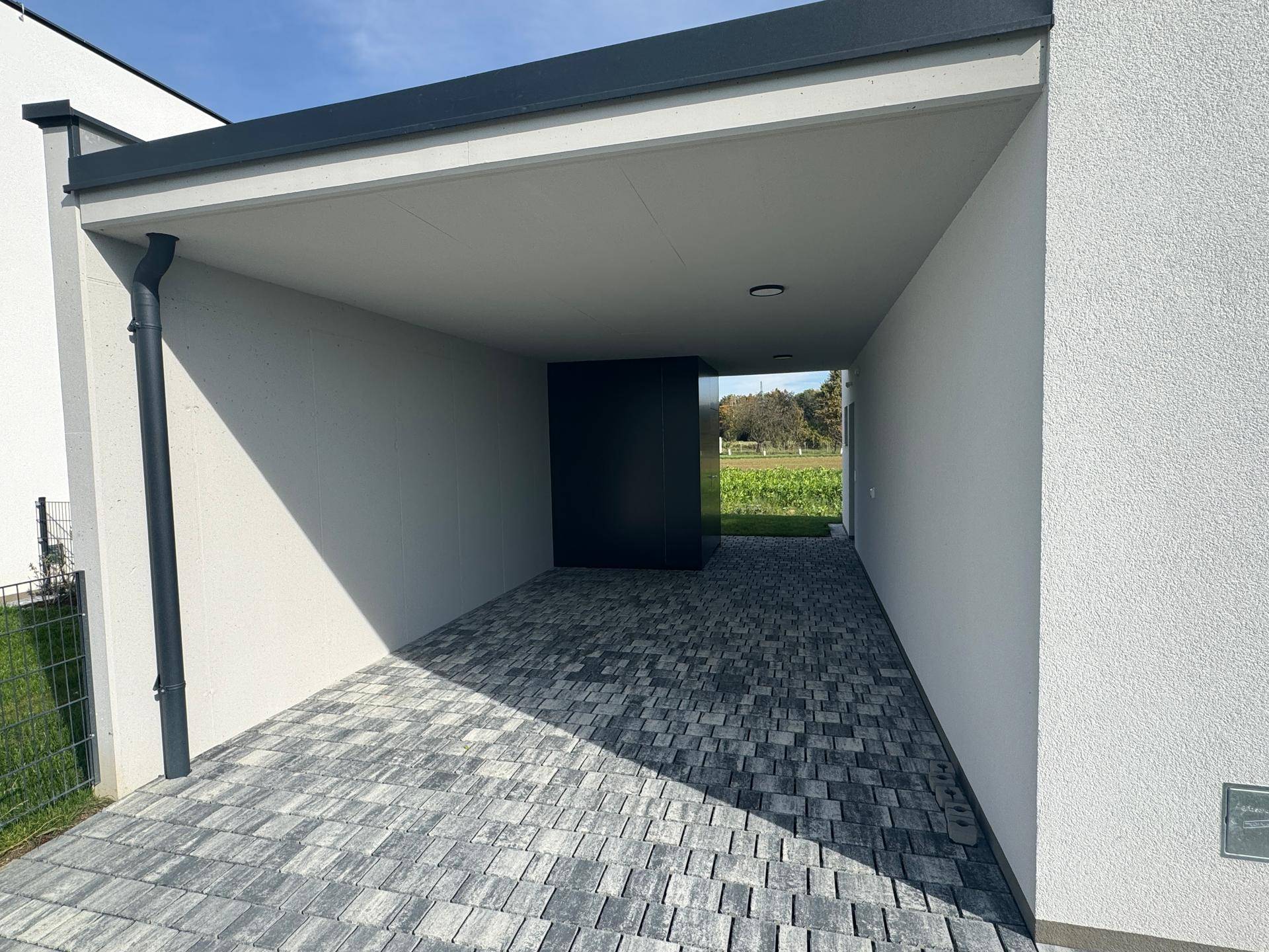 Geräumiger Carport mit gepflastertem Boden und Blick auf die umliegenden Felder.