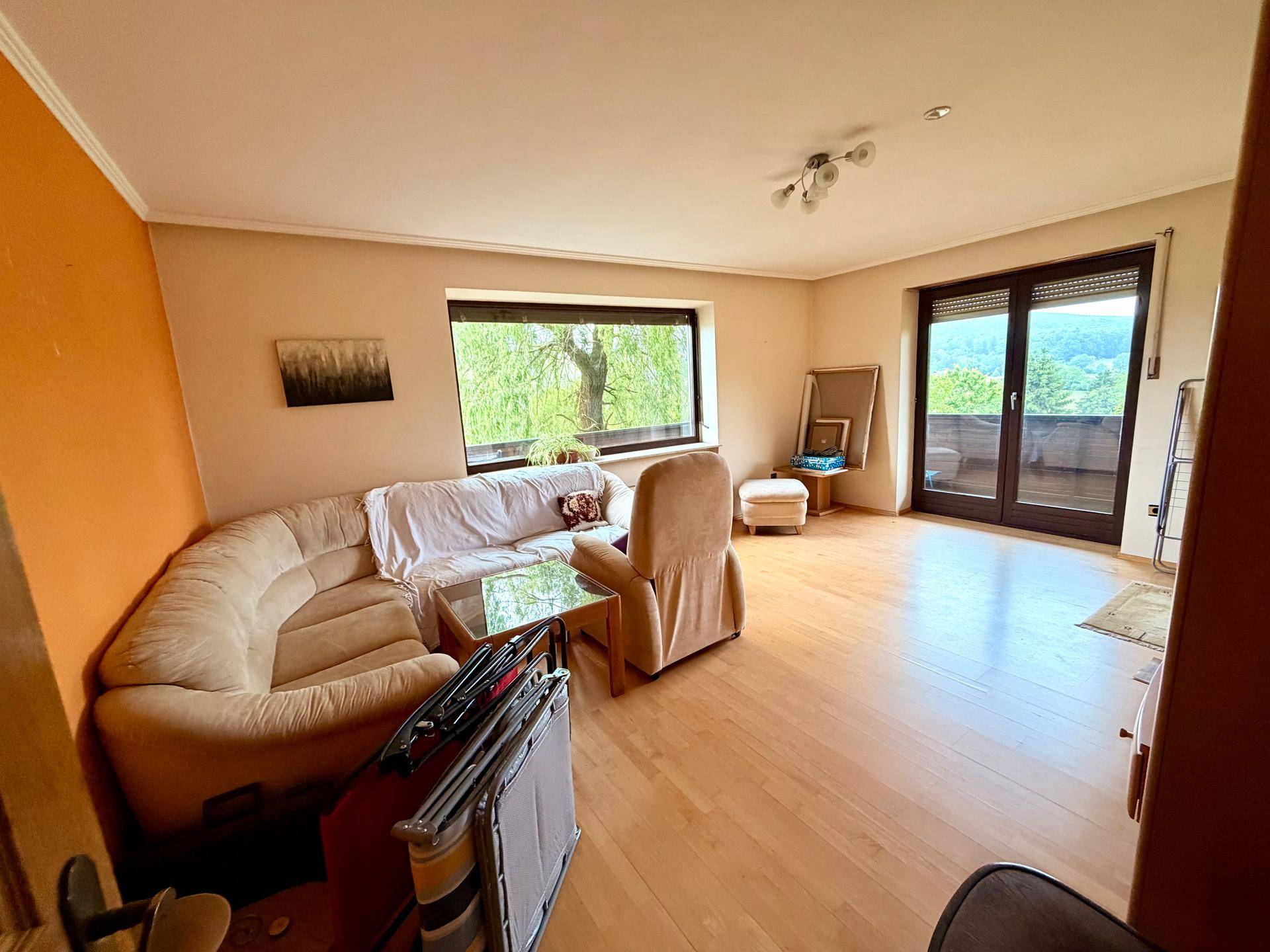 Helles Wohnzimmer mit beiger Eckcouch, Laminatboden und Zugang zum Balkon mit Weitblick.