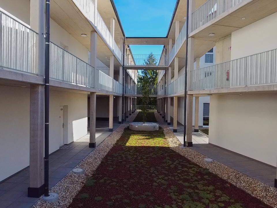Begrünter Innenhof zwischen modernen Gebäuden mit Wegen und Sitzgelegenheiten.