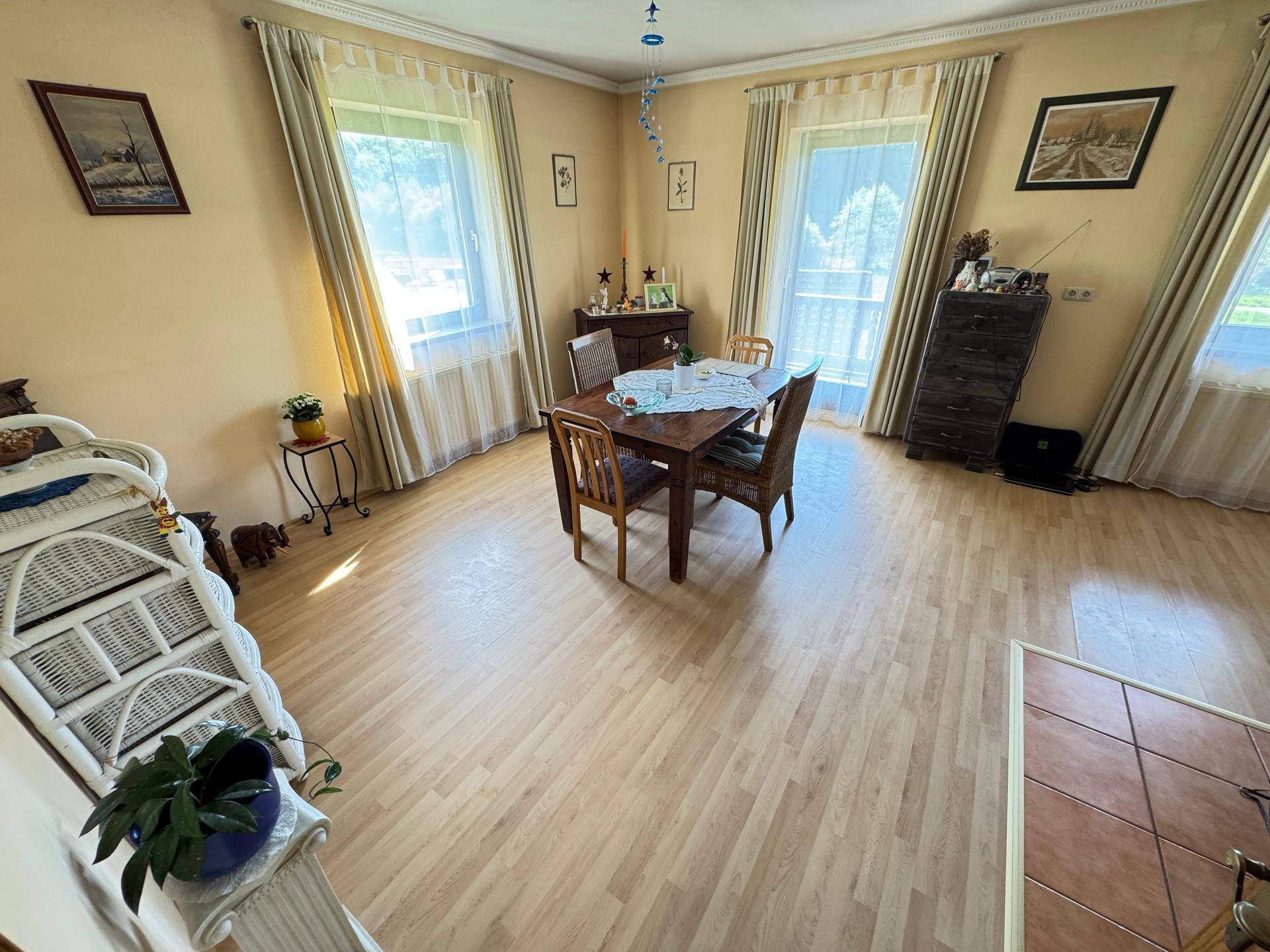 Heller Essbereich mit Laminatboden, Holztisch und Stühlen, umgeben von Fenstern mit Vorhängen.