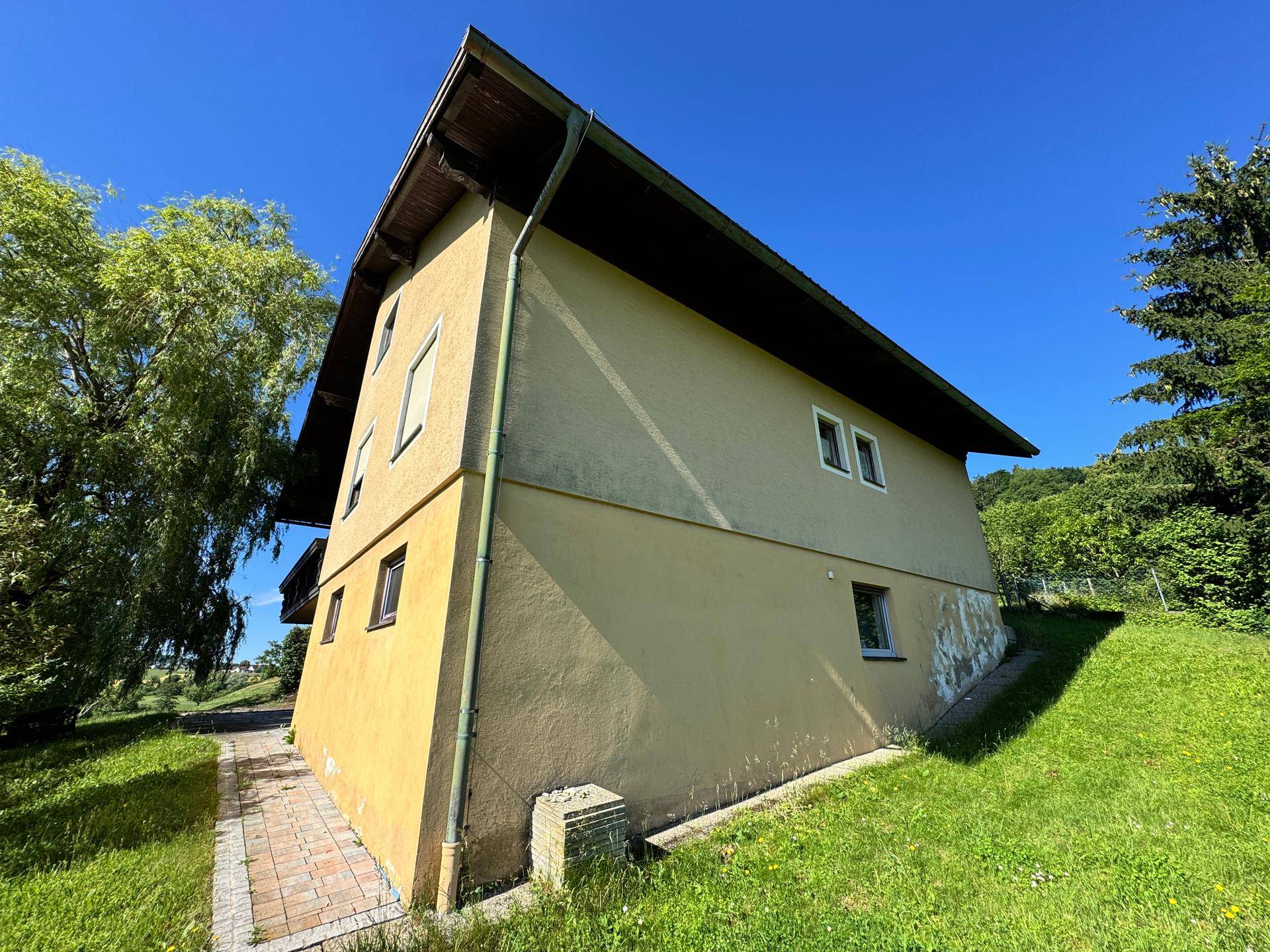 Seitenansicht des Hauses mit gepflastertem Weg und grüner Rasenfläche.