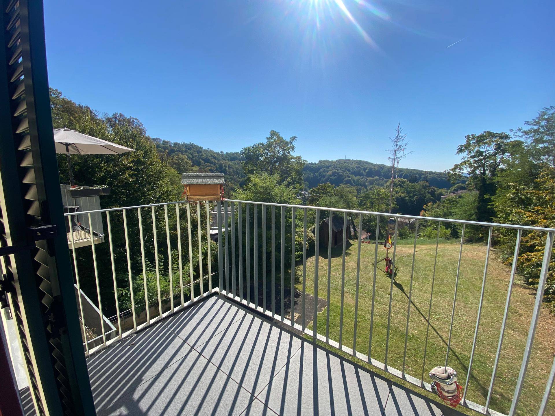Sonniger Balkon mit Fliesenboden und weitem Blick über grüne Hügel und Bäume.