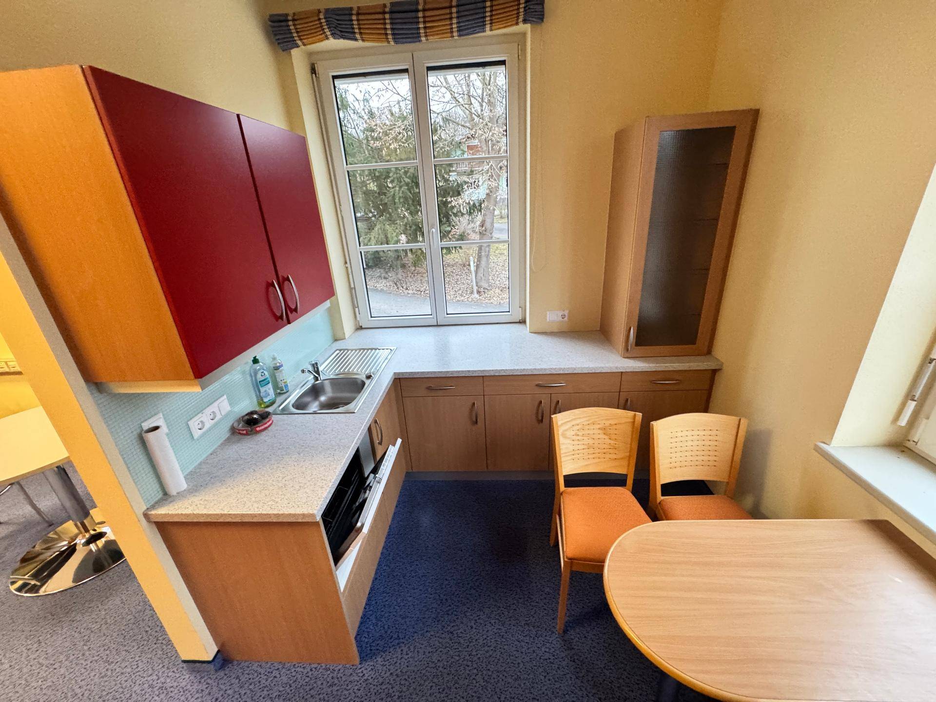 Kleine Küche mit Spüle, roten Oberschränken und Essbereich am Fenster.
