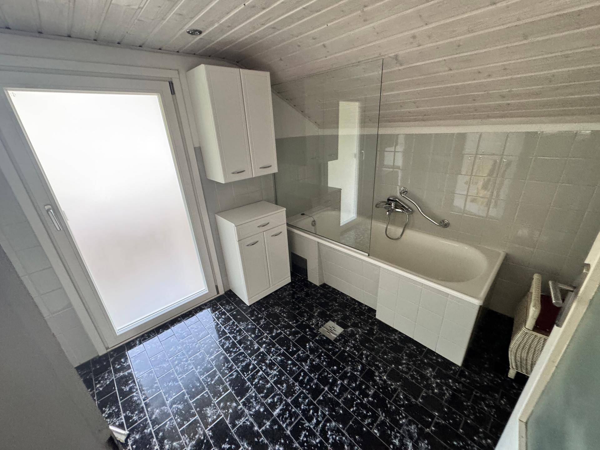Badezimmer mit schwarzem Fliesenboden, Badewanne und Holzdecke.