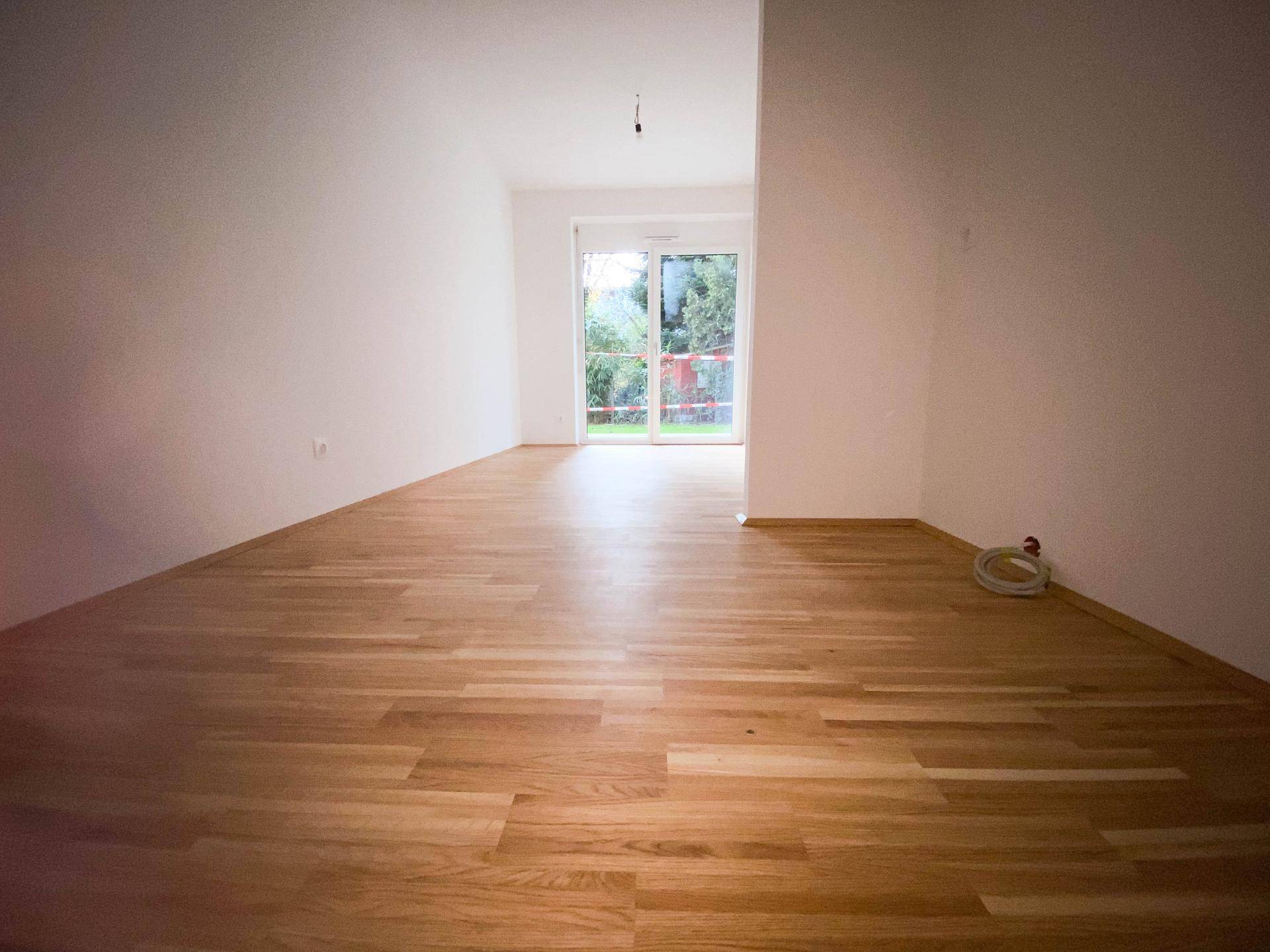 Geräumiger, heller Raum mit Parkettboden und Zugang zu einem Außenbereich durch große Fenster.