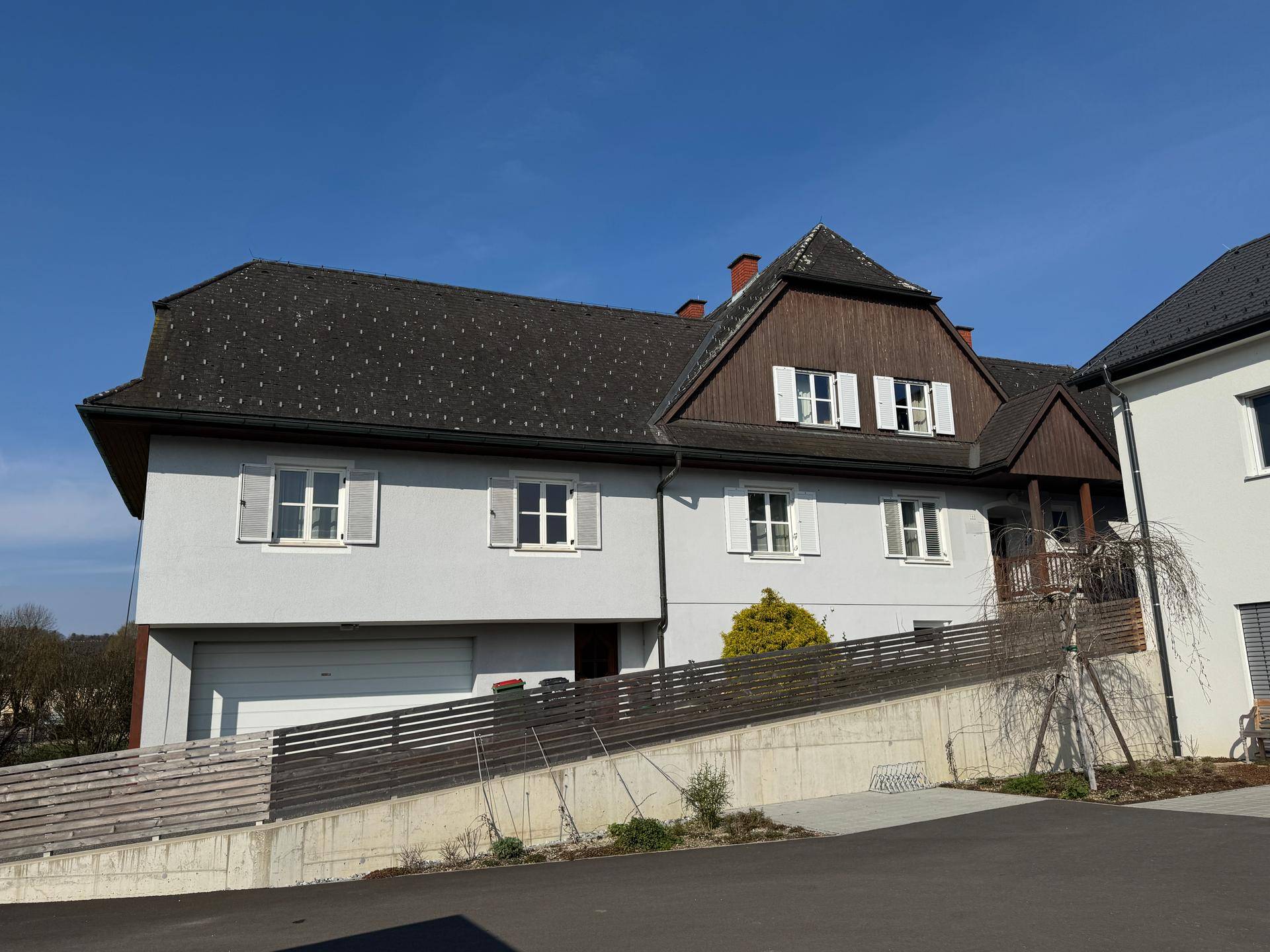 Vorderansicht des Hauses mit integrierter Garage und Zufahrt, umgeben von Grünflächen.