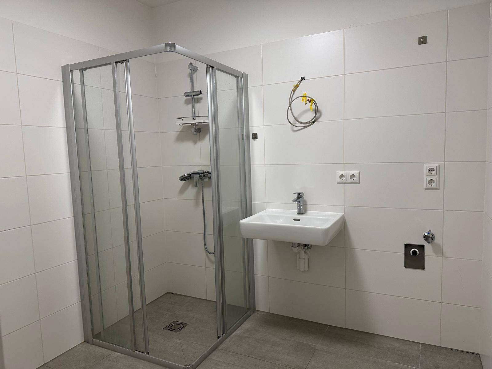 Modernes Badezimmer mit Eckdusche, Einzelwaschbecken und hellen Fliesen an Wänden und Boden.