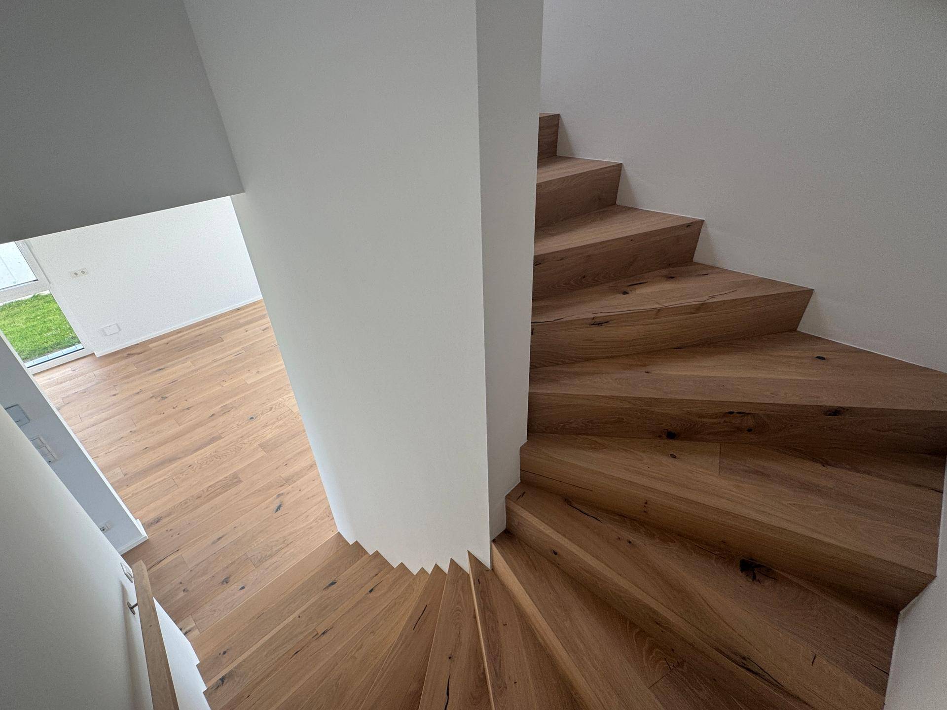 Moderne Holztreppe mit weiß gestrichenen Wänden, die in den oberen Bereich führt.