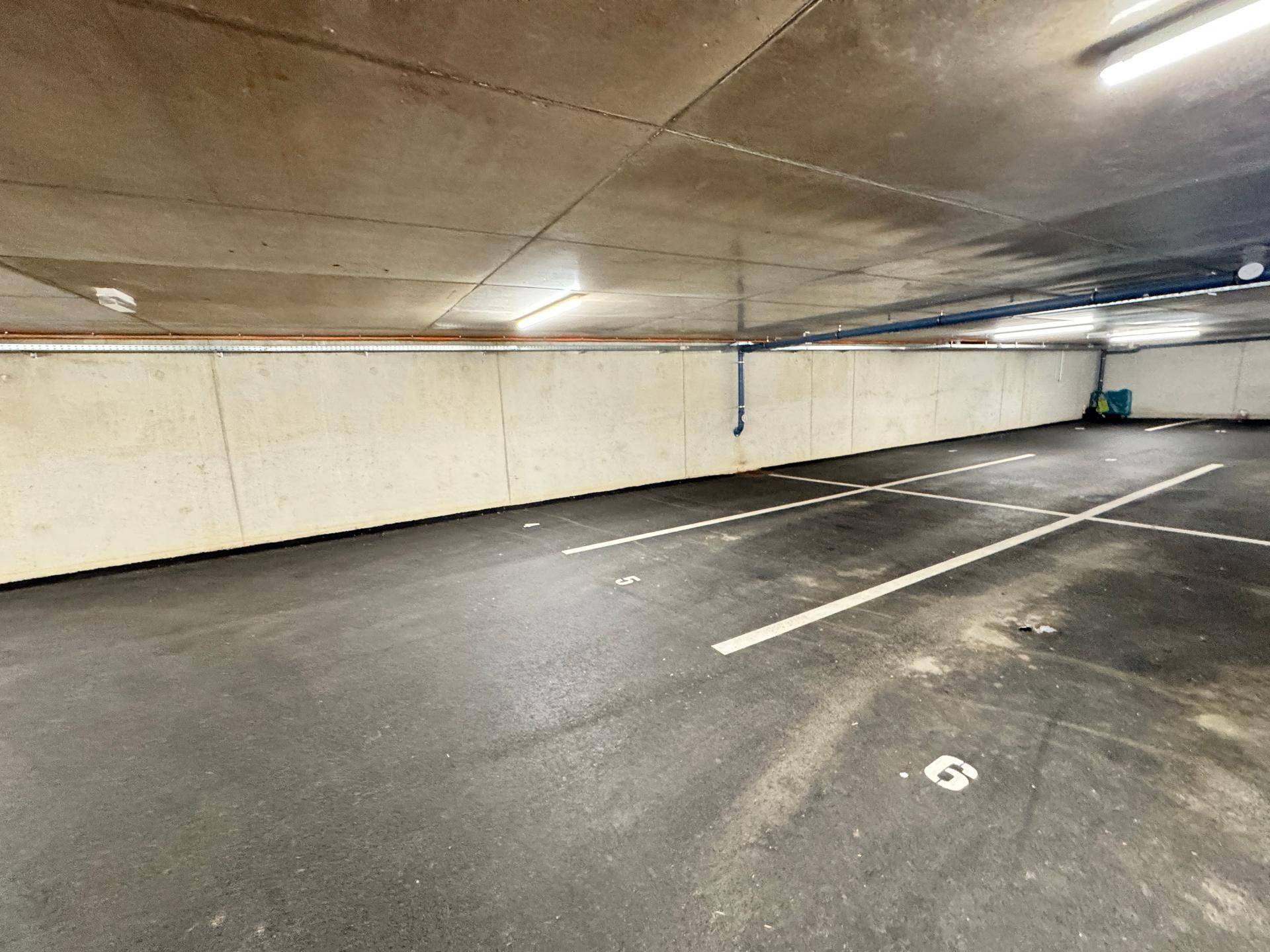 Leere Tiefgarage mit Betonwänden und markierten Parkplätzen, gut beleuchtet.
