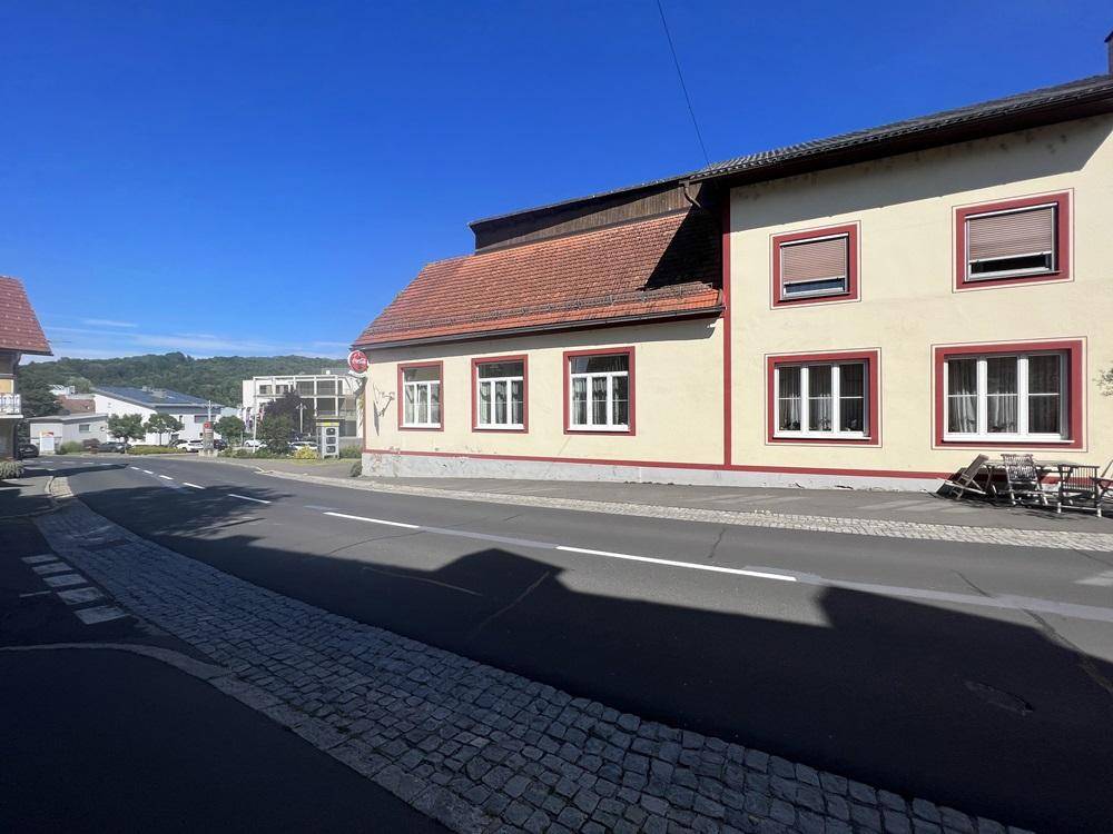 Seitenansicht des beigen Gebäudeteils mit weißen Fenstern und Rollläden an der Straße.