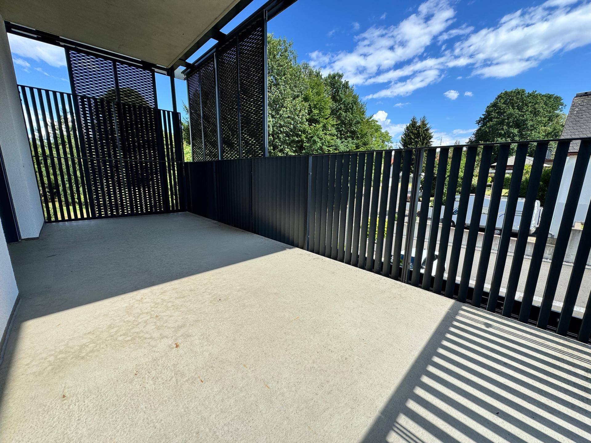 Geräumiger Balkon mit modernem schwarzen Geländer und Betonboden, ideal für Entspannung im Freien.