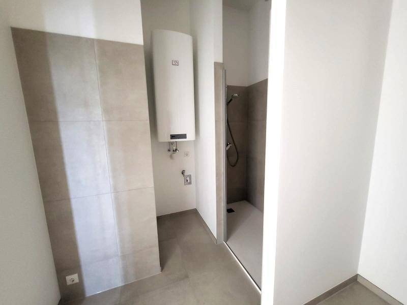 Modernes Badezimmer mit Duschbereich, Boiler und hellen Fliesen in einem Neubau.