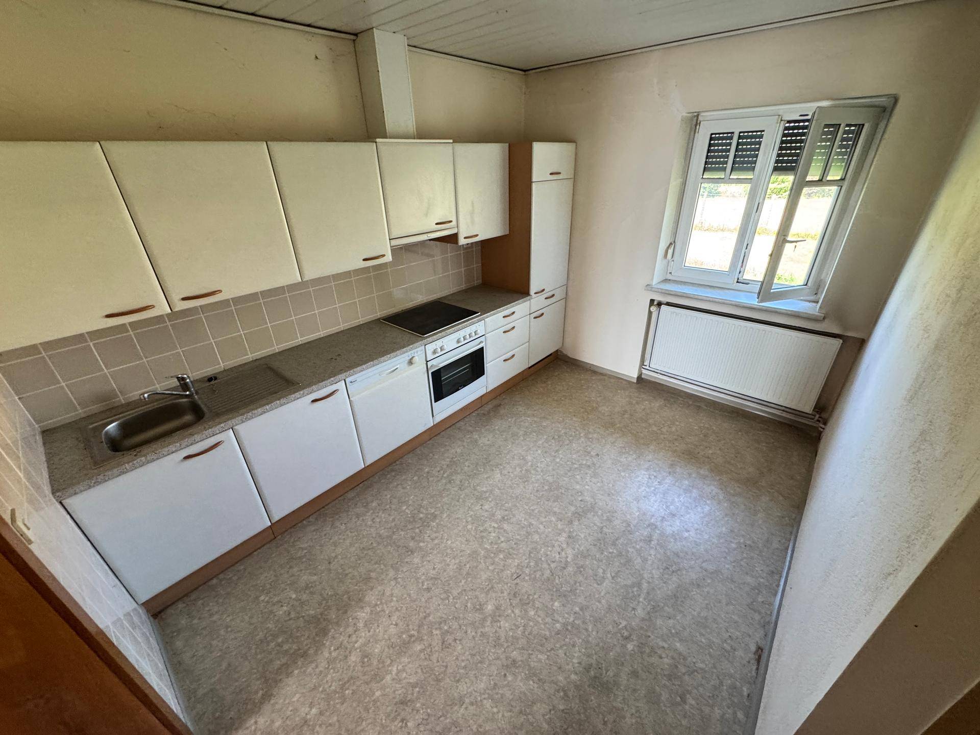 Kleine Einbauküche mit weißen Schränken, Spüle und Fensterblick.