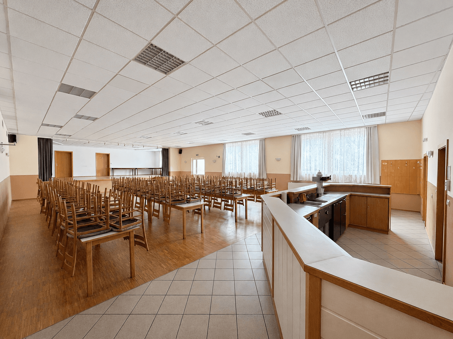 Ein großer Veranstaltungssaal mit Holzboden, vielen Stühlen und Tischen, bereit für Feierlichkeiten oder Konferenzen.