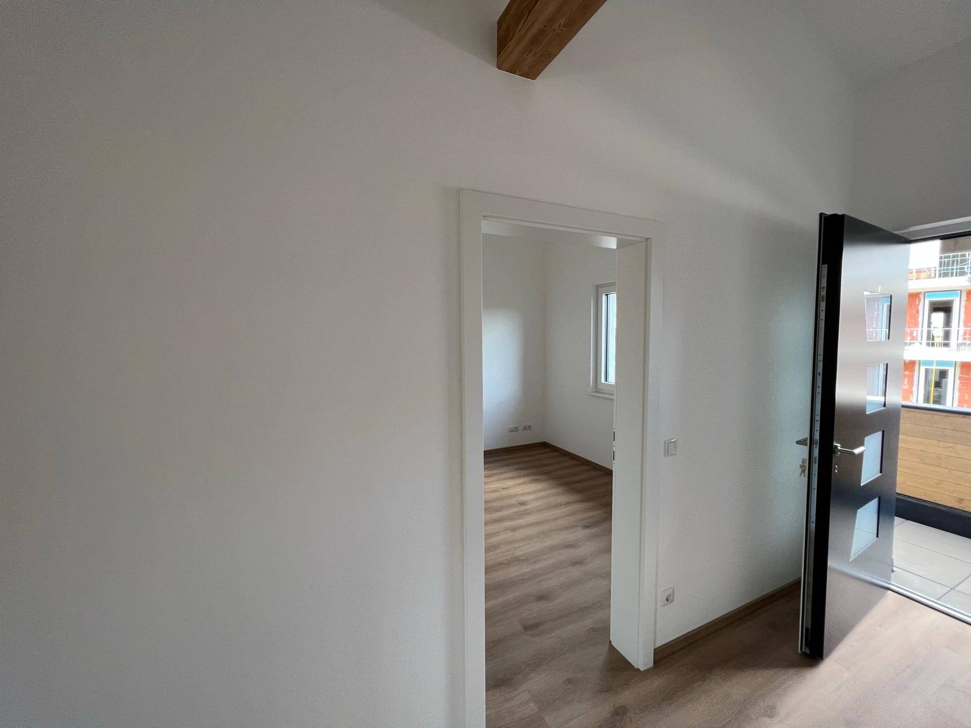 Heller Flur mit Laminatboden und Blick in ein angrenzendes Zimmer mit Fenster.