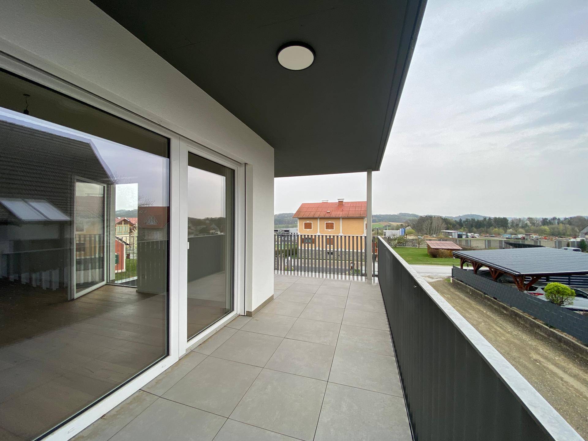 Geräumiger Balkon mit Fliesenboden und Blick auf die umliegende Landschaft und Häuser.