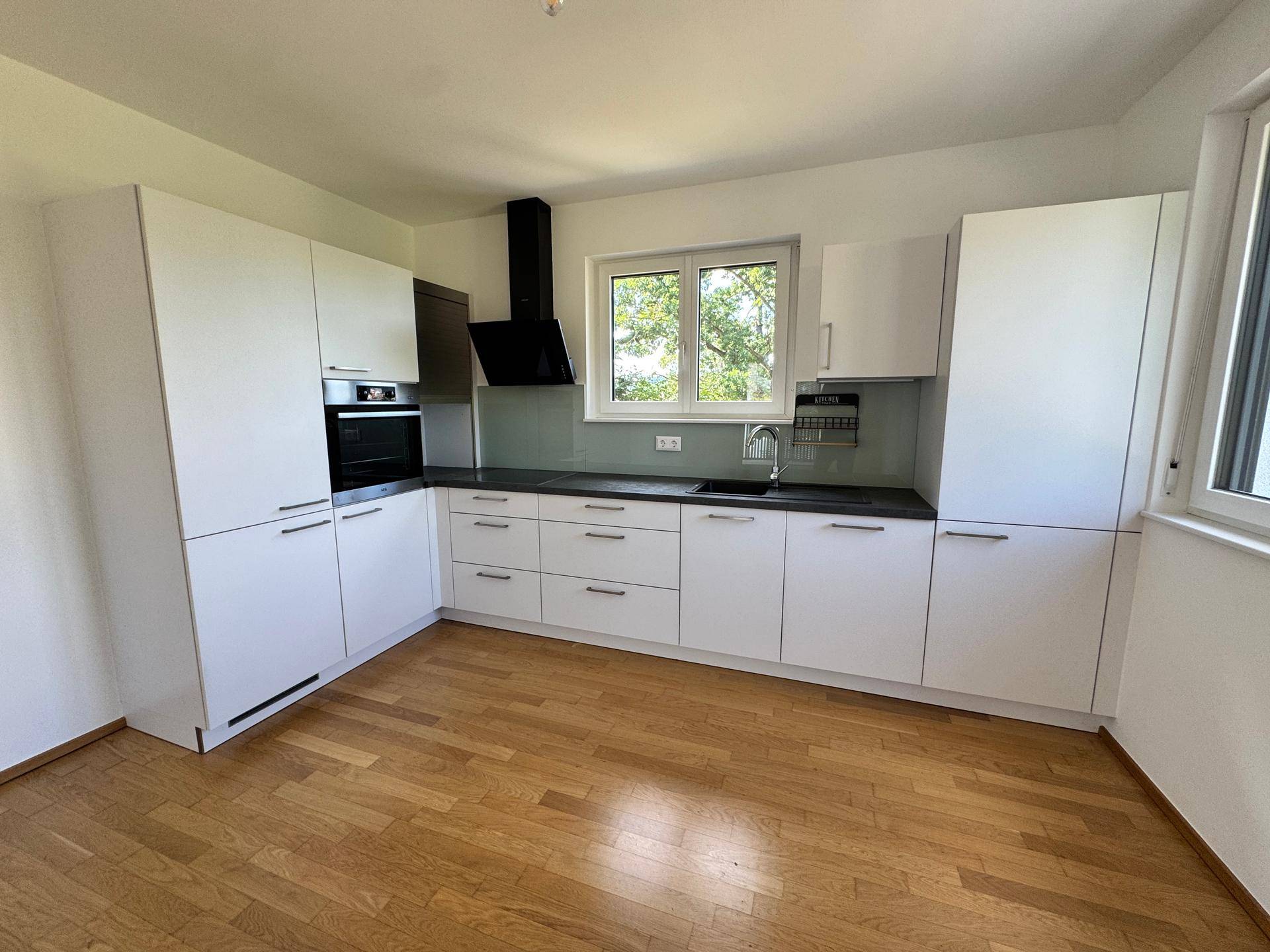Voll ausgestattete, moderne Einbauküche in Weiß mit dunkler Arbeitsplatte und Holzboden.
