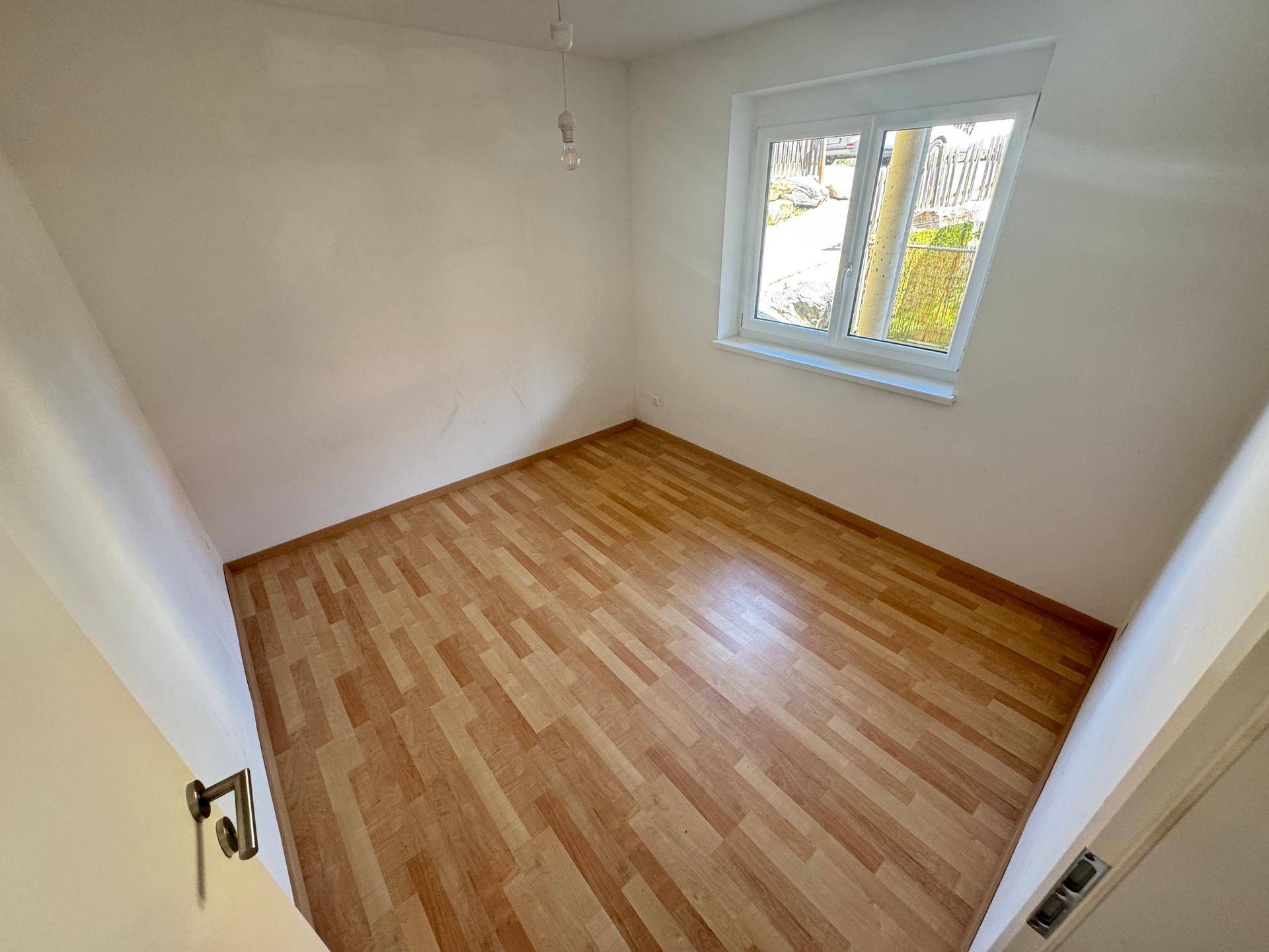 Helles Schlafzimmer mit Laminatboden und einem Fenster, das viel Tageslicht hereinlässt.