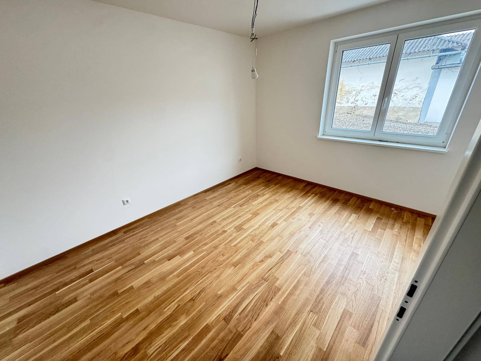 Helles Schlafzimmer mit neuem Parkettboden und einem Fenster mit Blick auf die Umgebung.