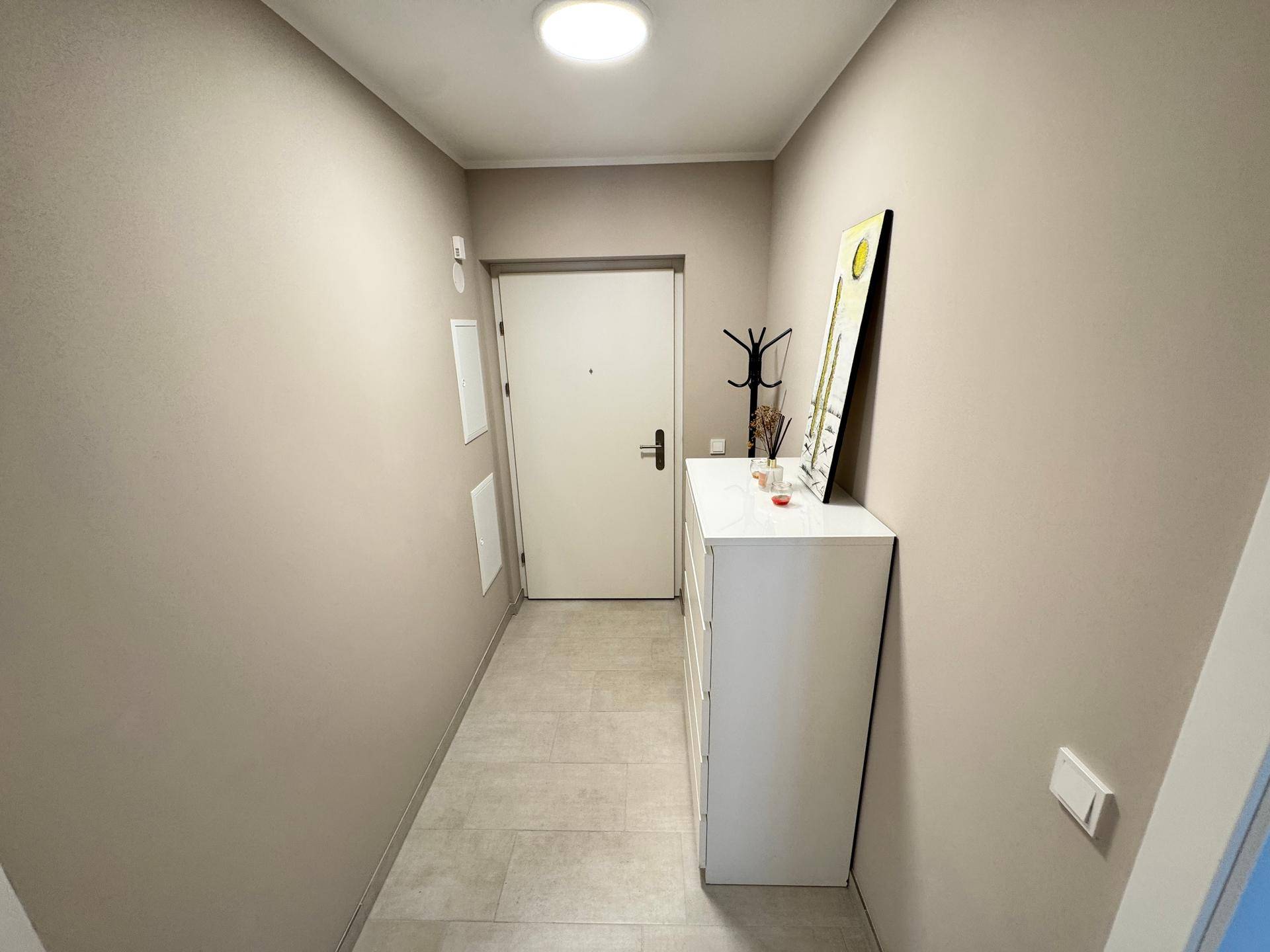 Eingangsbereich mit heller Fliese, weißer Kommode und Garderobe neben der Wohnungstür.