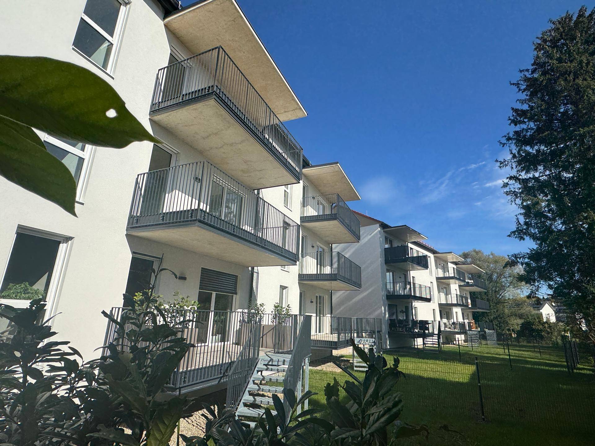 Neubau-Wohngebäude mit modernen Balkonen und gepflegter Rasenfläche an einem sonnigen Tag.