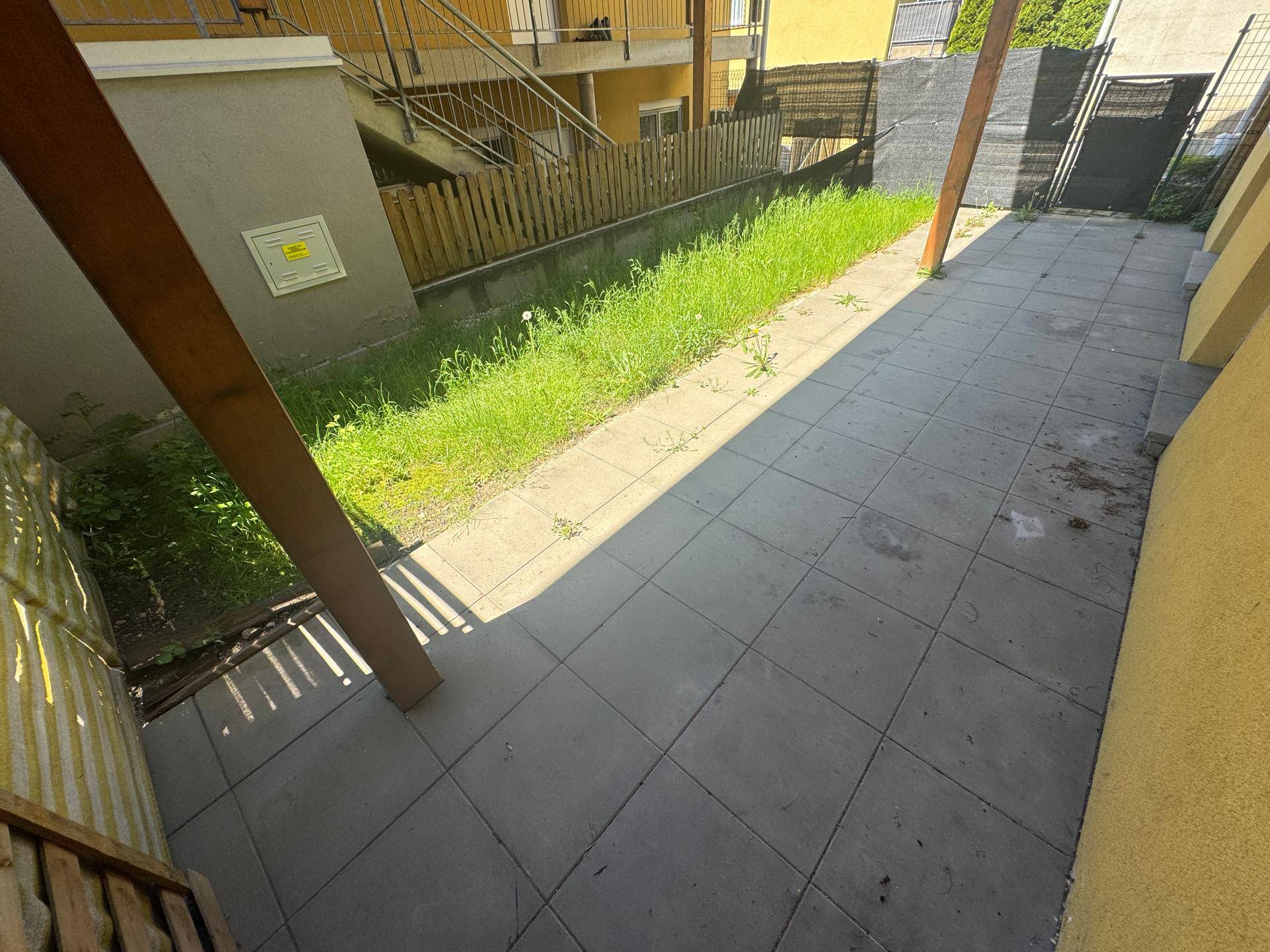 Gepflasterte Terrasse mit angrenzendem Rasenstreifen und Holzzaun im Außenbereich.