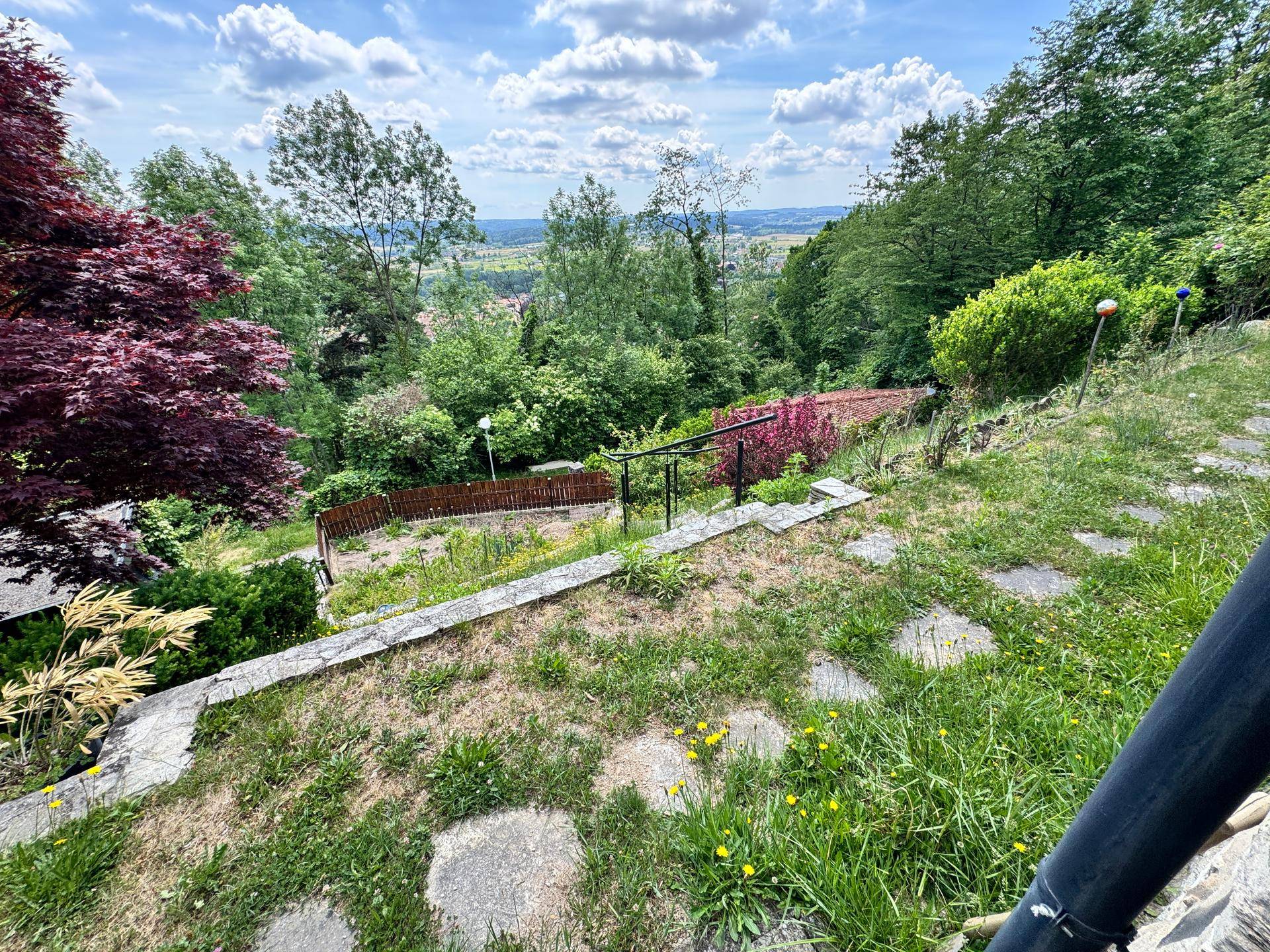 Terrassierter Gartenbereich mit Steinstufen und üppigem Grün, bietet einen weiten Blick über die Landschaft.