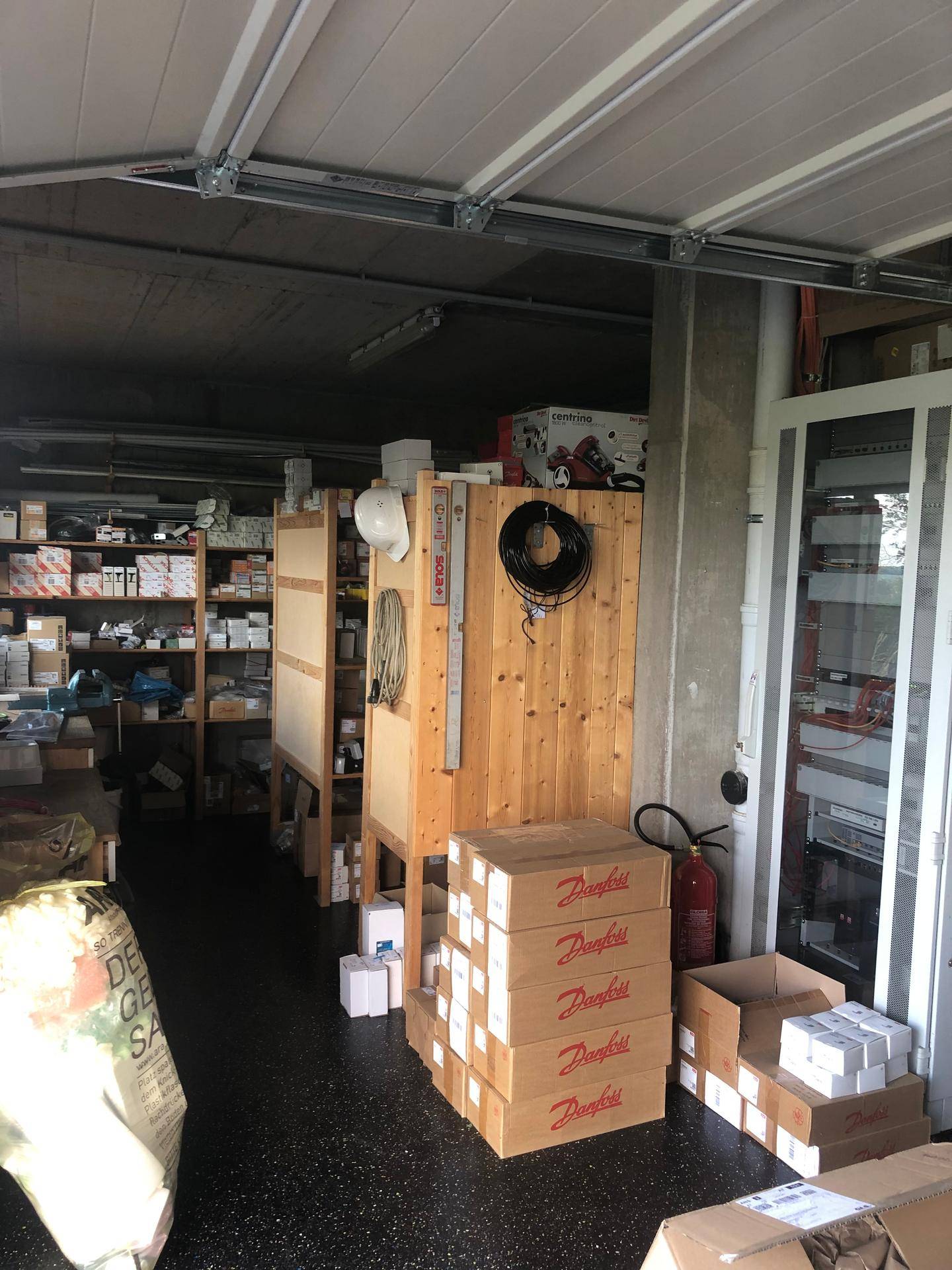 Lagerraum mit Regalen, Kartons und verschiedenen Materialien unter einer Garagendecke.