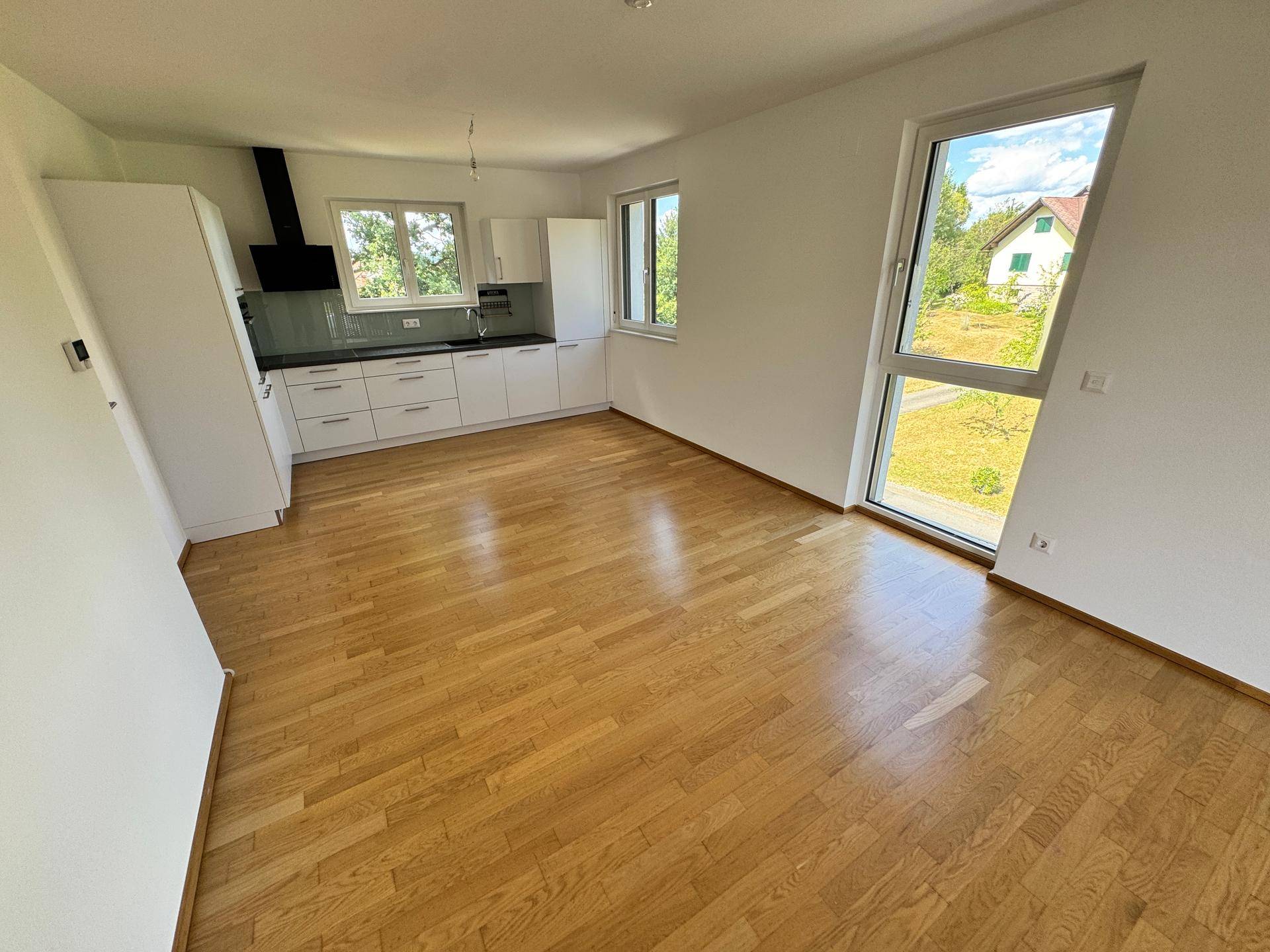 Offener Wohnbereich mit neuer Einbauküche, Holzboden und großen Fenstern mit Blick ins Grüne.