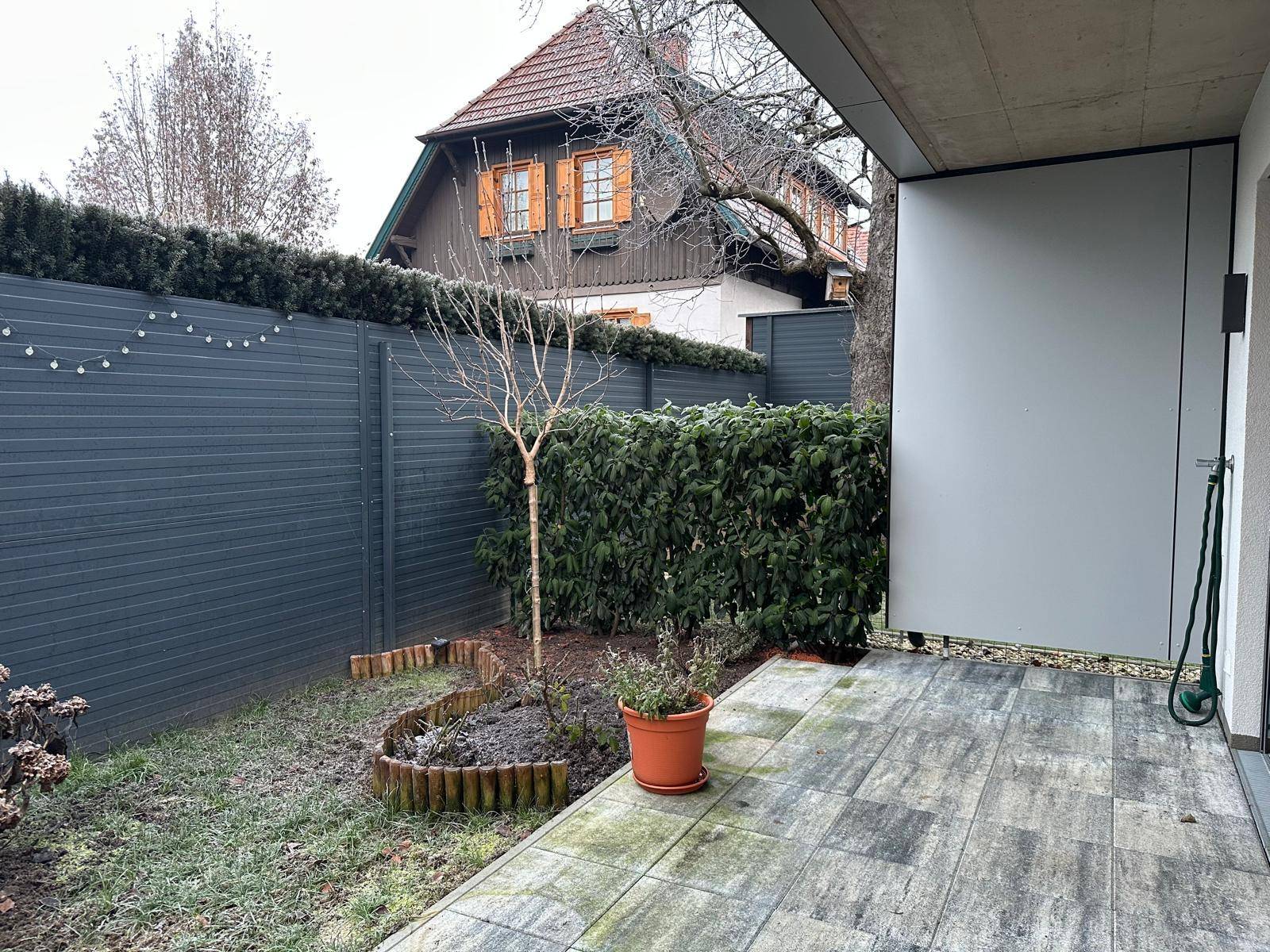 Gemütliche Terrasse mit Steinplatten und kleinem Gartenbereich, umgeben von einer Hecke.