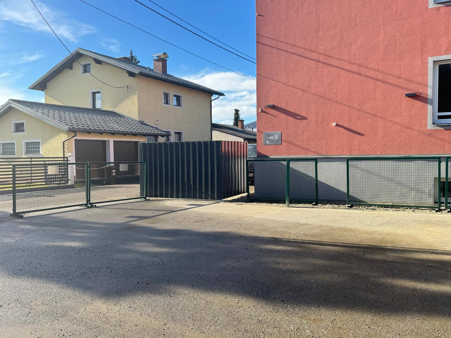 Rotes Wohngebäude neben einem gelben Haus mit Zaun und Zufahrt.