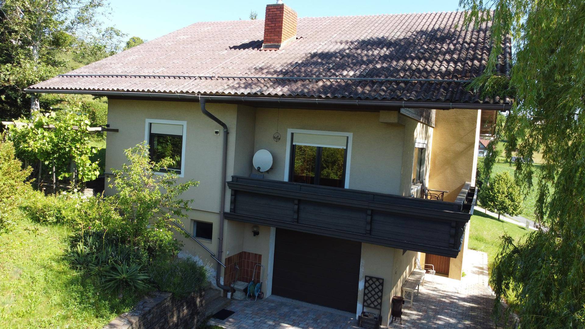 Ansicht des Hauses von oben mit Satteldach, Balkon und umgebender grüner Landschaft.