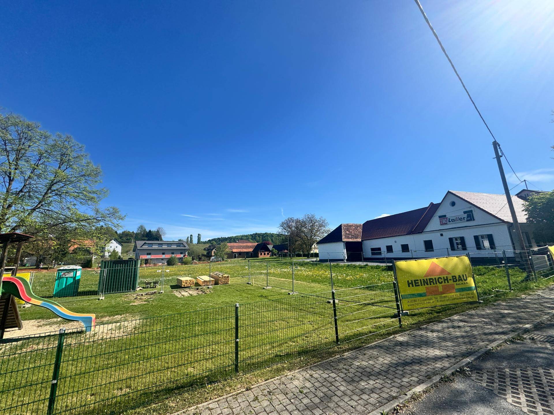 Außenansicht eines Grundstücks mit Spielplatz und Blick auf umliegende Gebäude unter blauem Himmel.