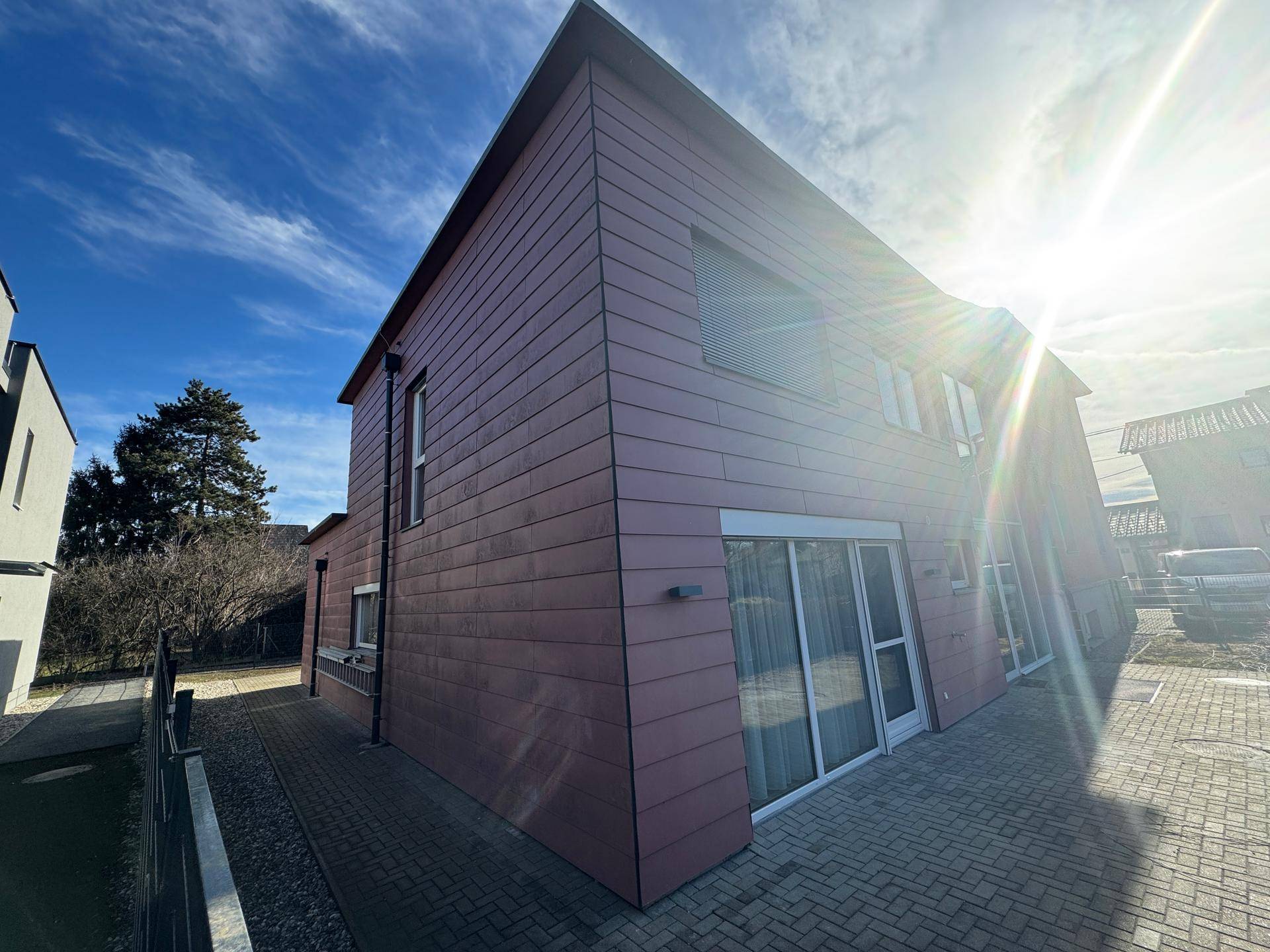 Modernes Gebäude mit roter Fassade und großen Fenstern unter strahlendem Himmel.