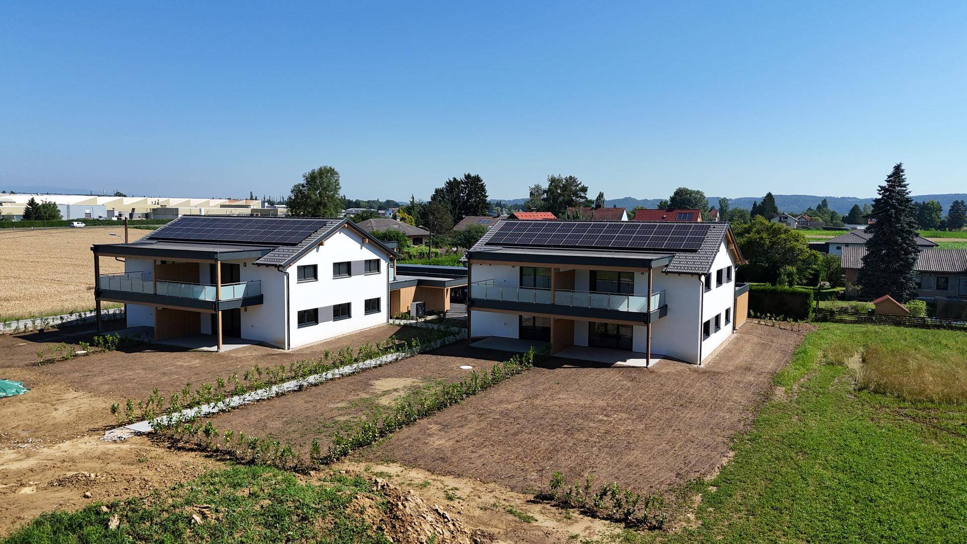 Luftaufnahme von zwei modernen Doppelhaushälften mit Solaranlagen in ländlicher Umgebung.