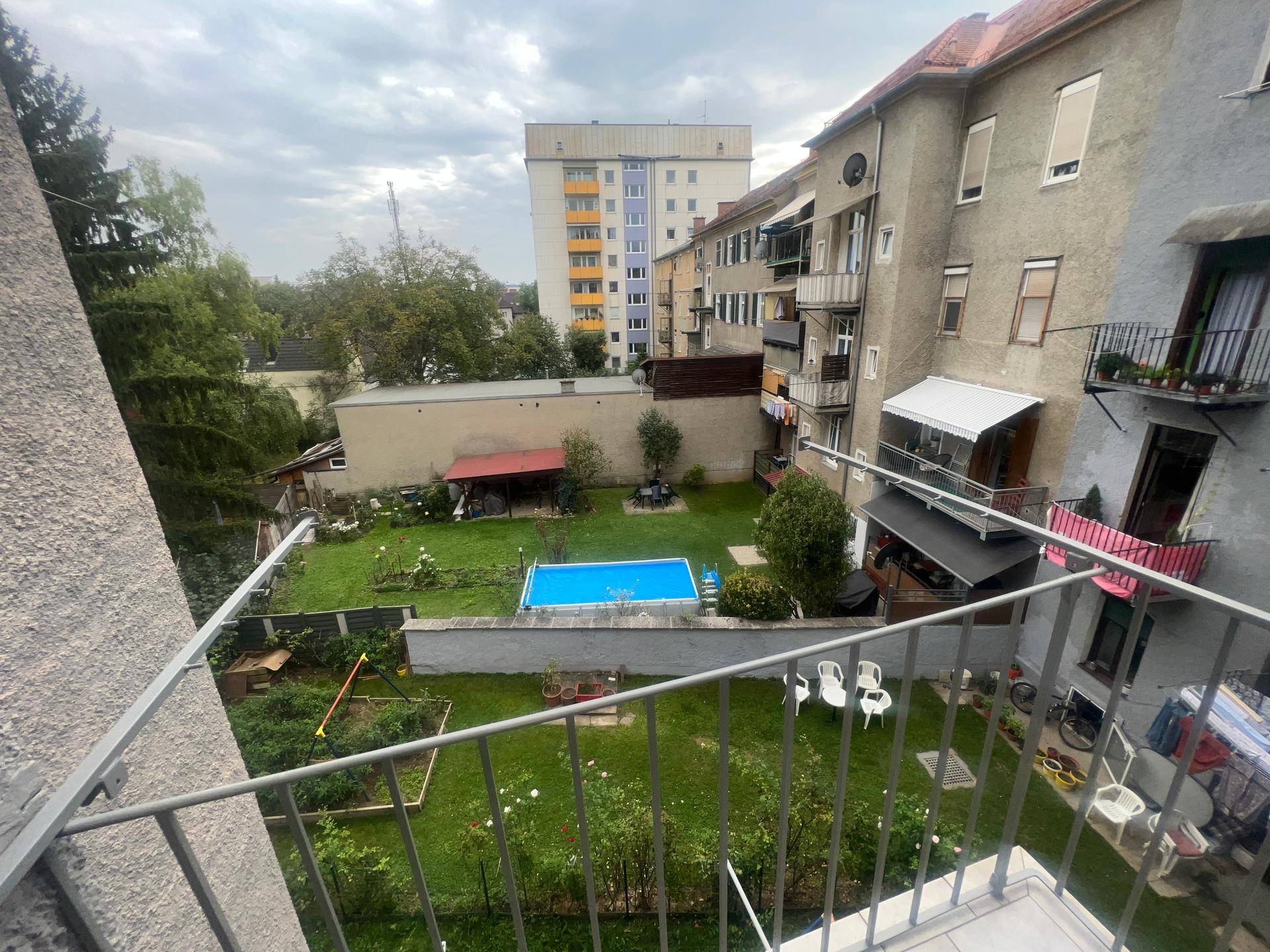 Balkon mit Blick auf einen grünen Gartenbereich mit kleinem Pool und Spielplatz.