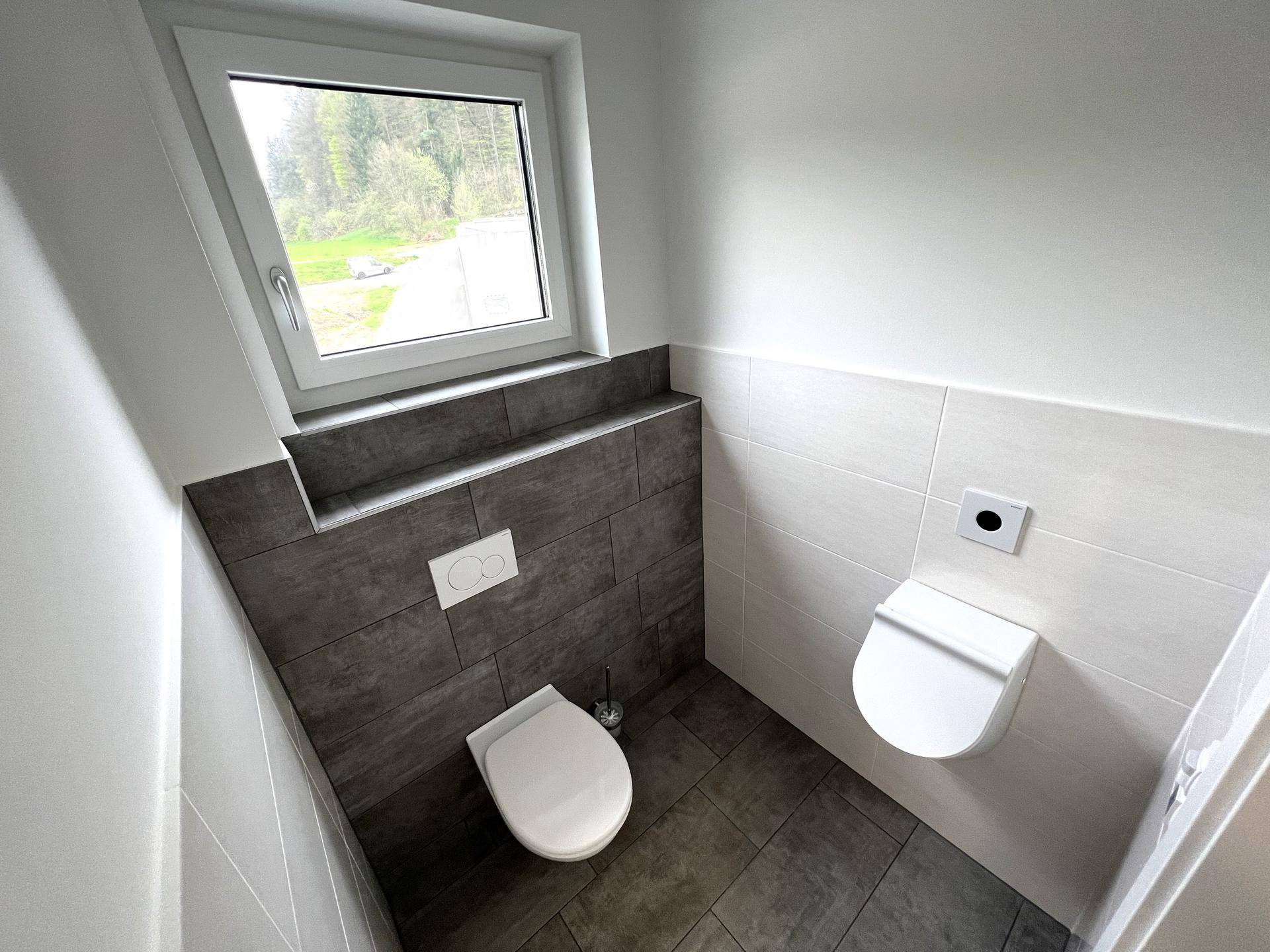 Modernes Gäste-WC mit dunklen und hellen Fliesen, wandhängender Toilette und Fenster.
