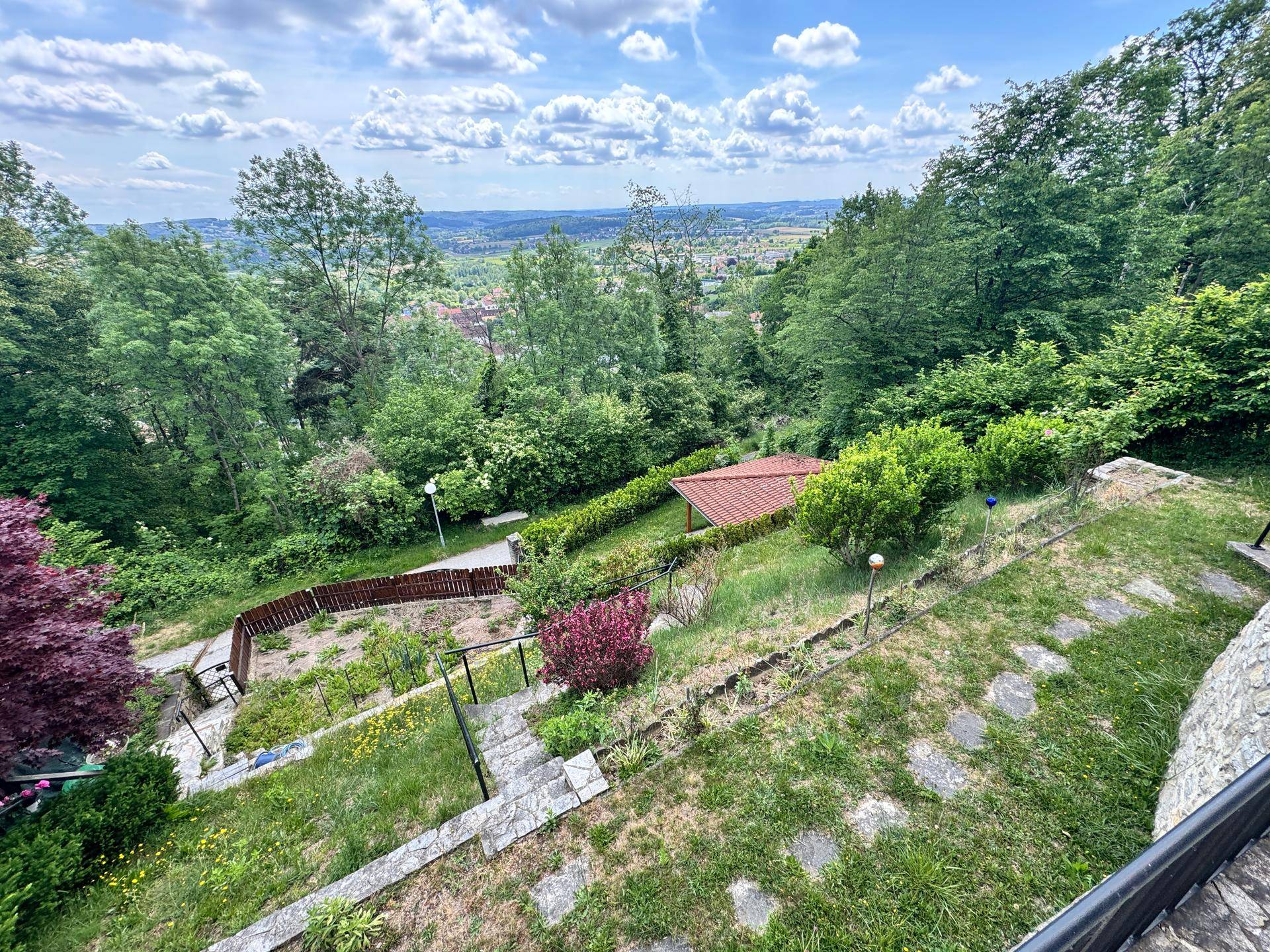 Terrassierter Garten mit Steintreppen, Rasenflächen und einem kleinen Gartenhaus im Hintergrund.