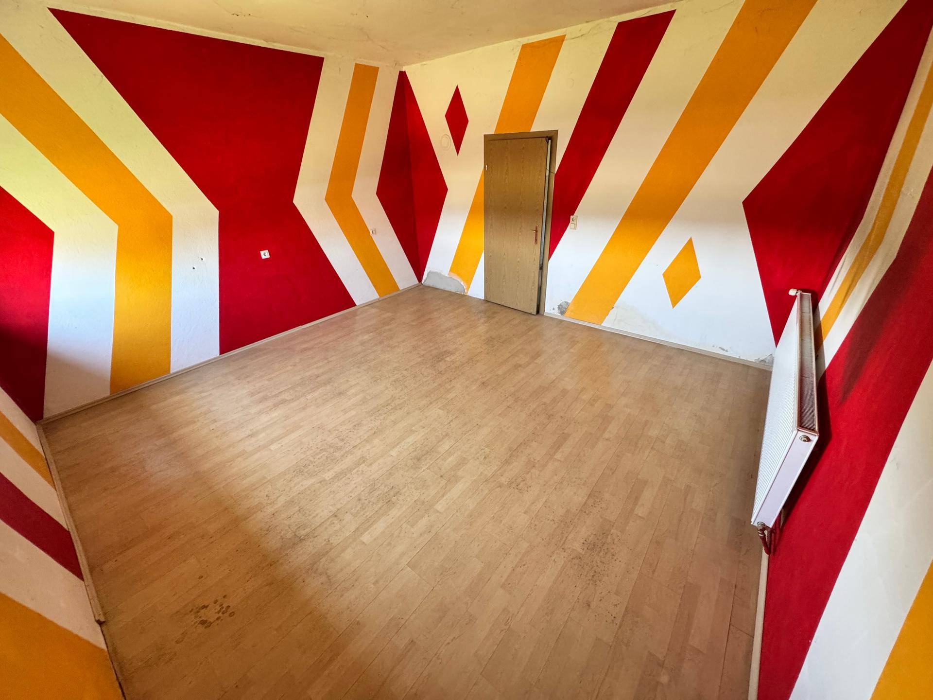 Kinderzimmer mit auffälliger Wandgestaltung in Rot und Gelb und Holzfußboden.
