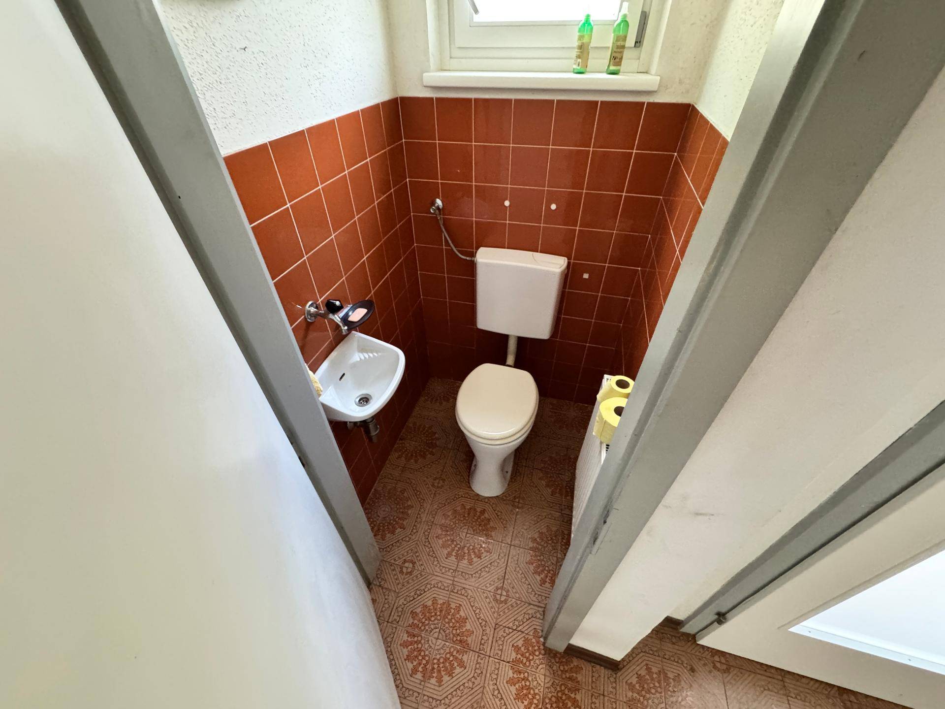 Kleines Gäste-WC mit Terrakotta-Fliesen, Toilette und Waschbecken.