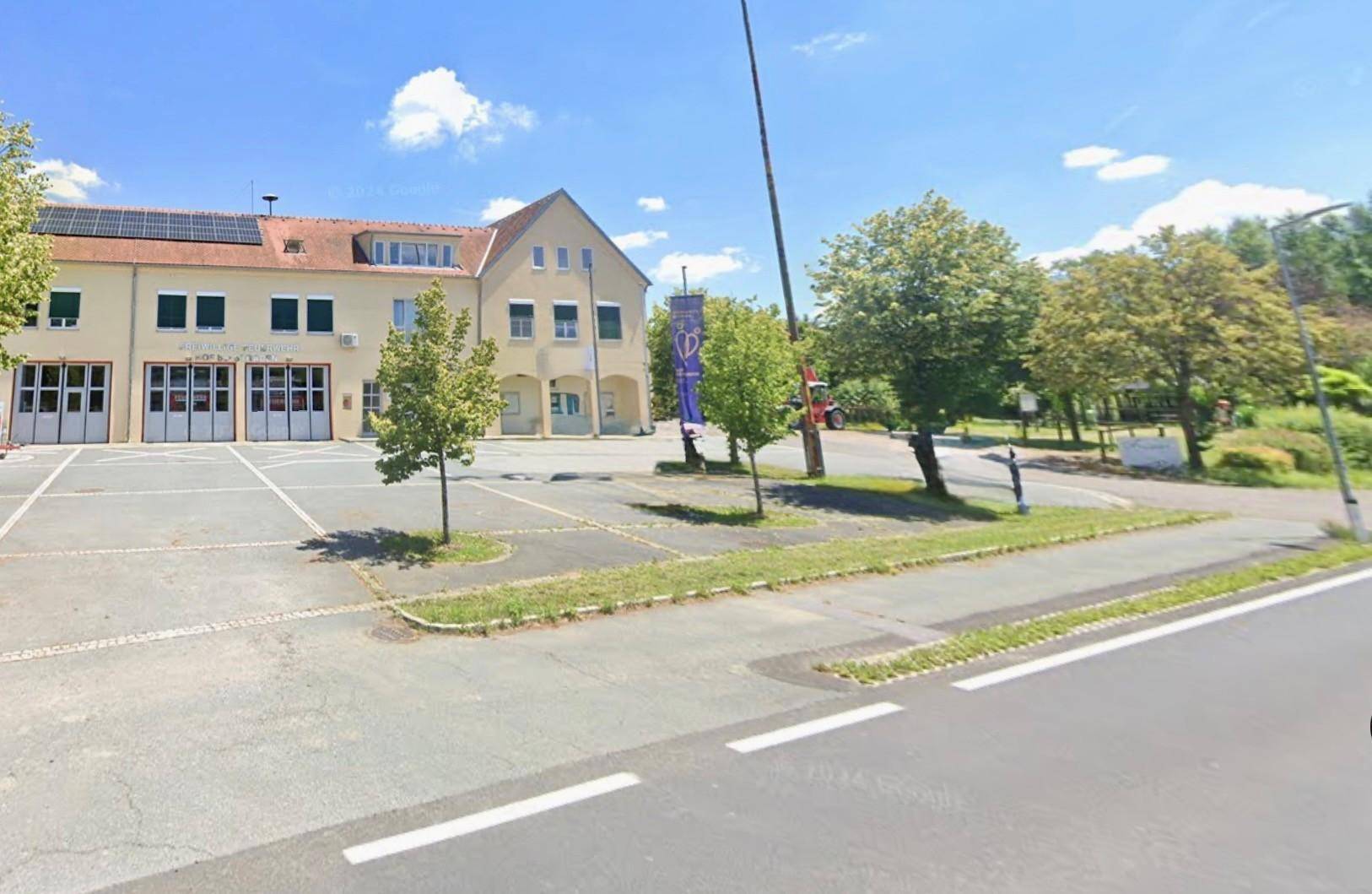 Außenansicht eines Gebäudes mit Parkplätzen und Bäumen unter blauem Himmel.