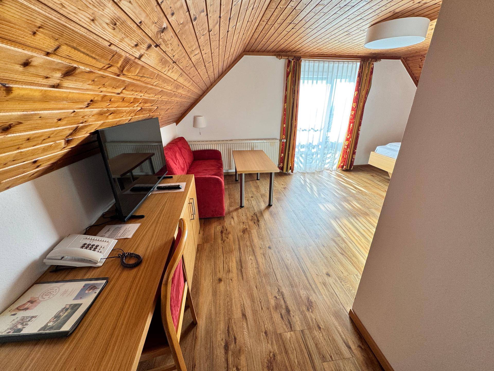 Schlafzimmer mit Holzbalkendecke, Schreibtisch und Fernseher.