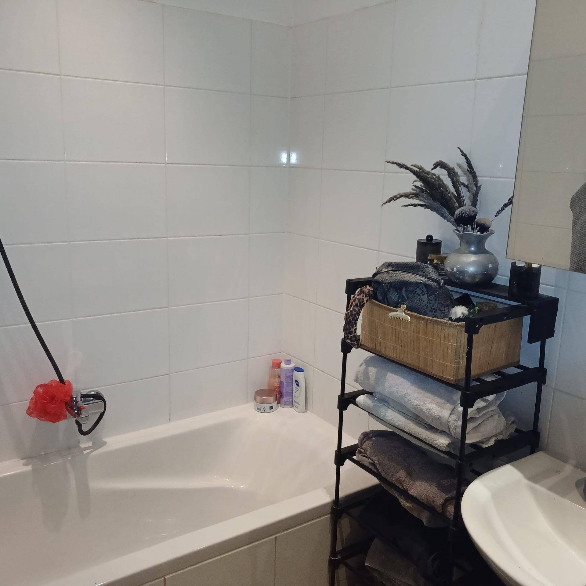 Badezimmer mit Badewanne, weißen Fliesen und einem praktischen Regal für Handtücher und Pflegeprodukte.