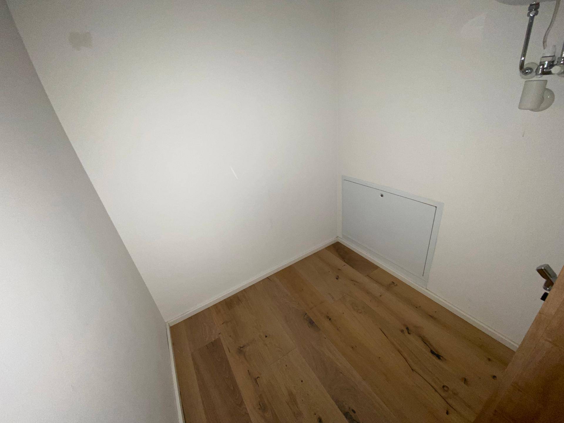 Kleiner Abstellraum mit Holzboden und weiß gestrichenen Wänden, ideal für Lagerung.