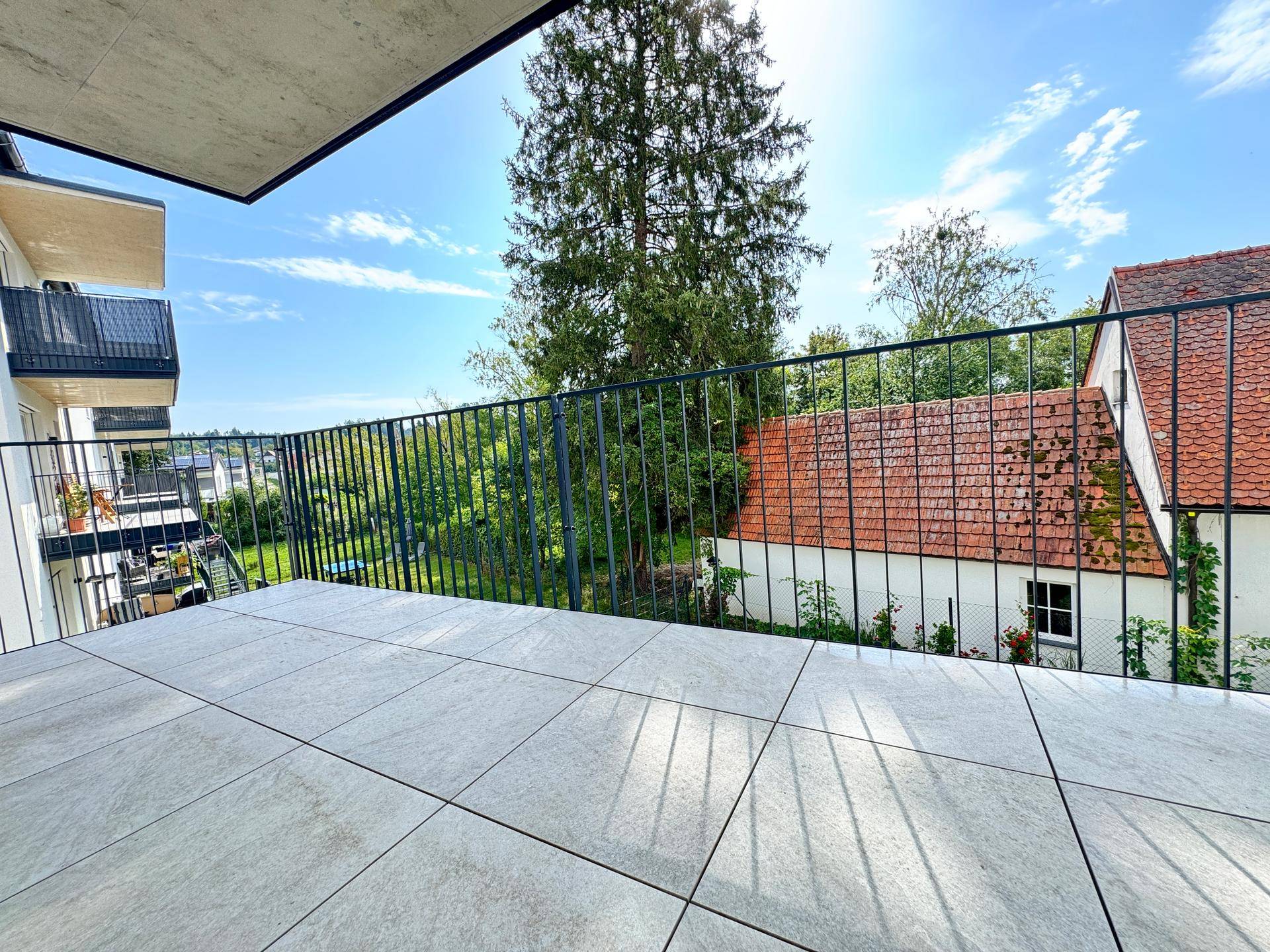 Großer Balkon mit Fliesenboden und Blick auf grüne Bäume und Dächer.