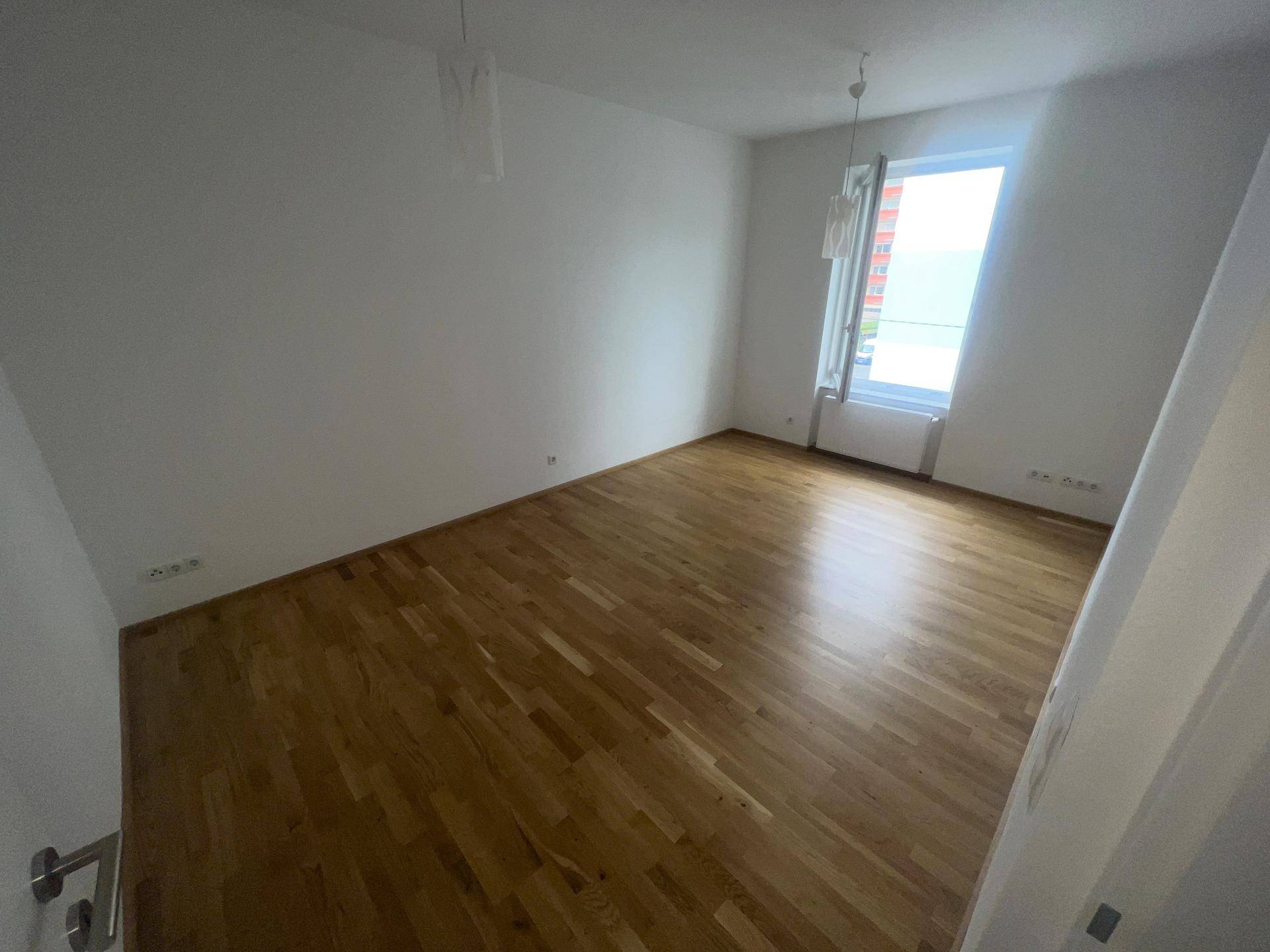 Geräumiges Schlafzimmer mit Parkettboden und einem großen Fenster für viel Tageslicht.