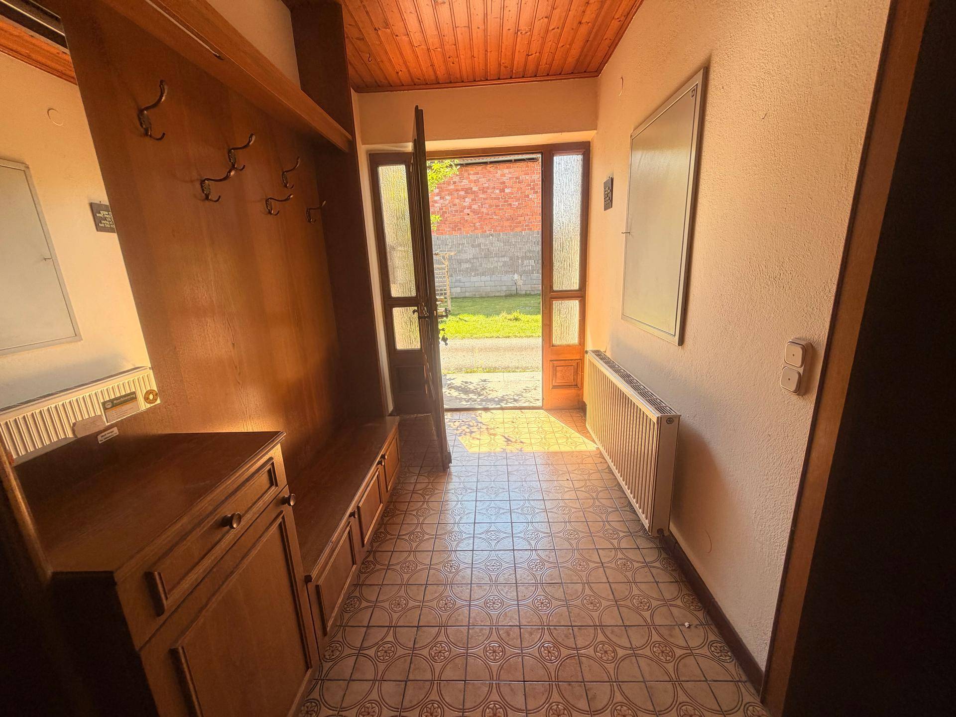 Heller Eingangsbereich mit gefliestem Boden, Holzdecke und Garderobe.