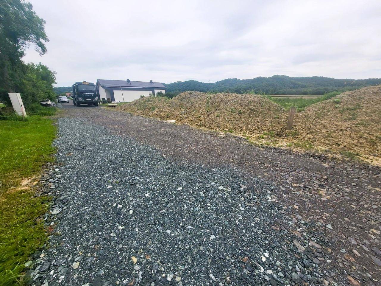 Schotterweg führt zu einem Haus in ländlicher Umgebung mit Hügeln im Hintergrund.