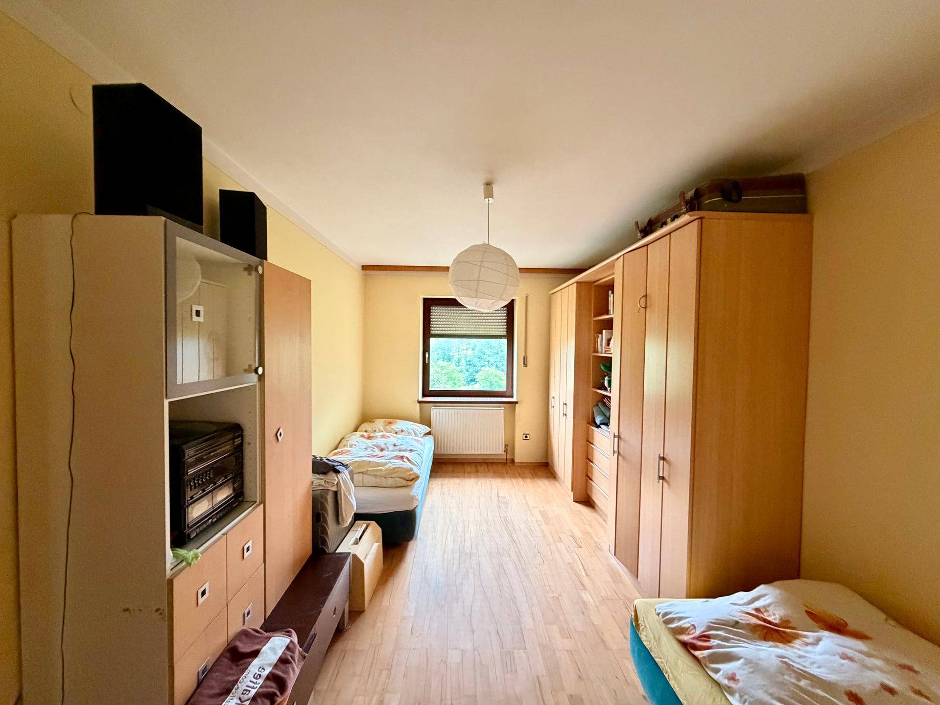 Schlafzimmer mit zwei Einzelbetten, Laminatboden und Holzschränken, hell und funktional eingerichtet.